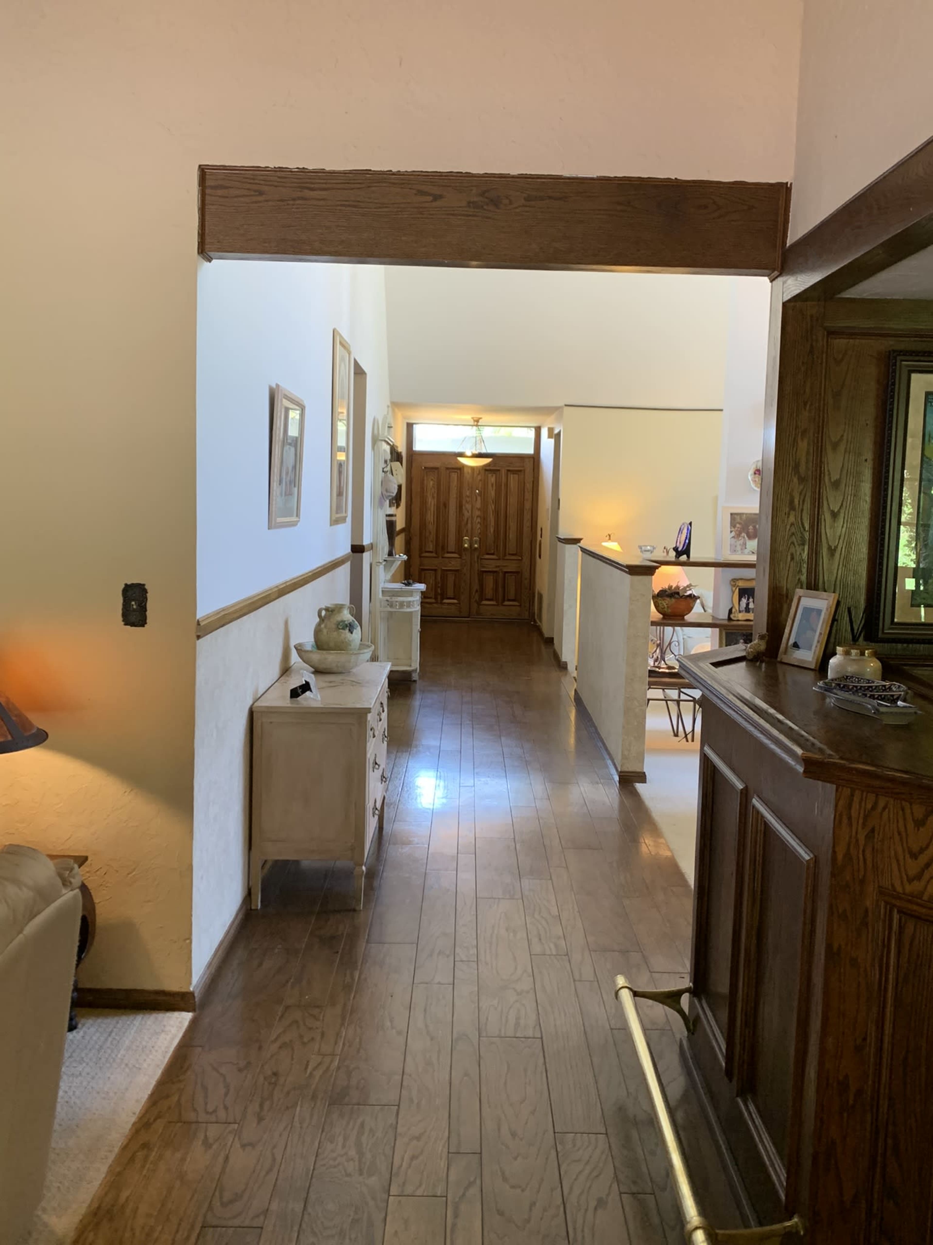 A wooden-floored hallway leading to a doorway with double doors at the end, flanked by light-colored walls and decor.