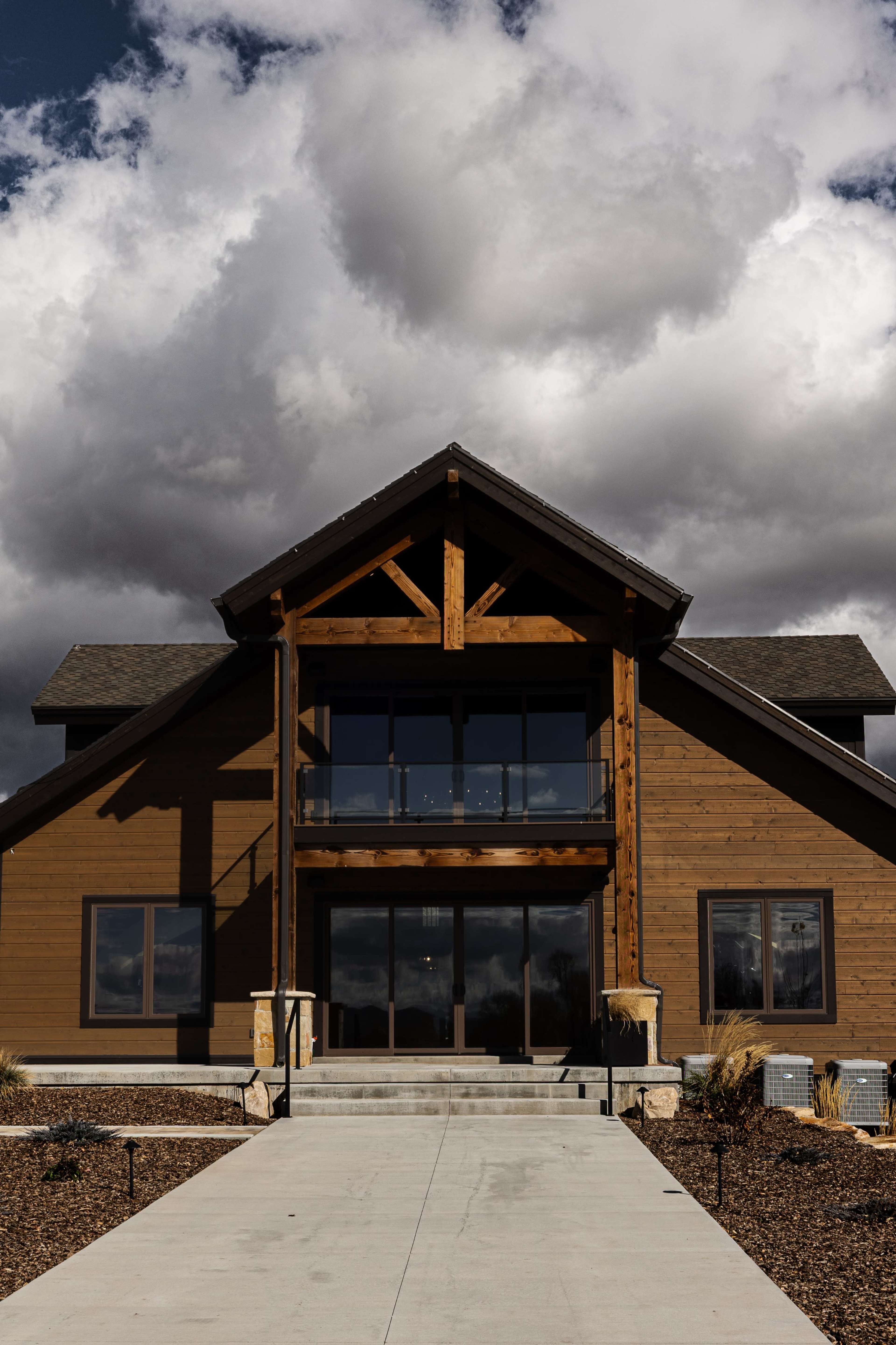 A large wooden house with a prominent triangular roof and a spacious entryway stands against a backdrop of dramatic clouds.