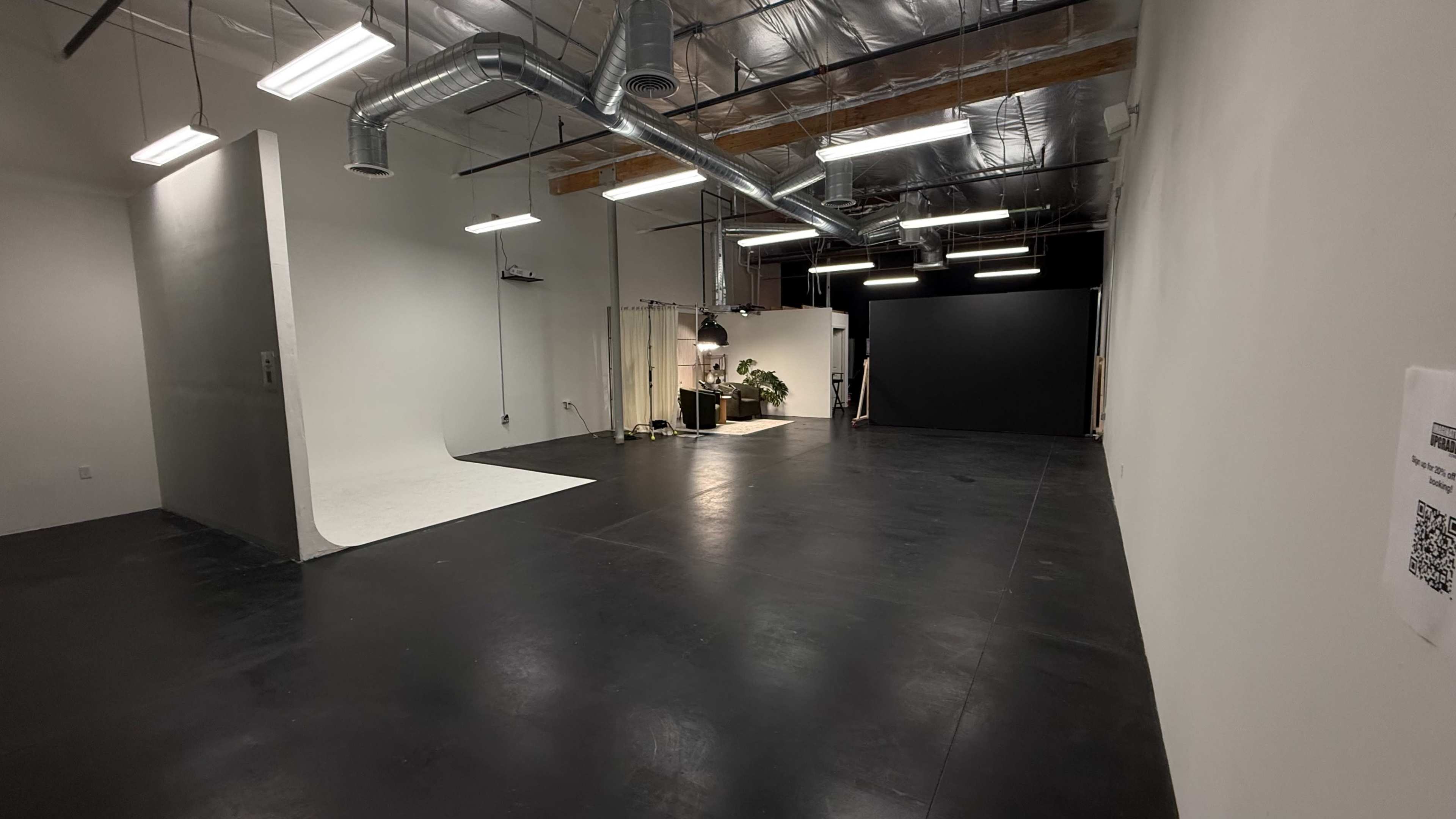 The image shows a spacious studio with a seamless backdrop, modern lighting fixtures, and a black floor.