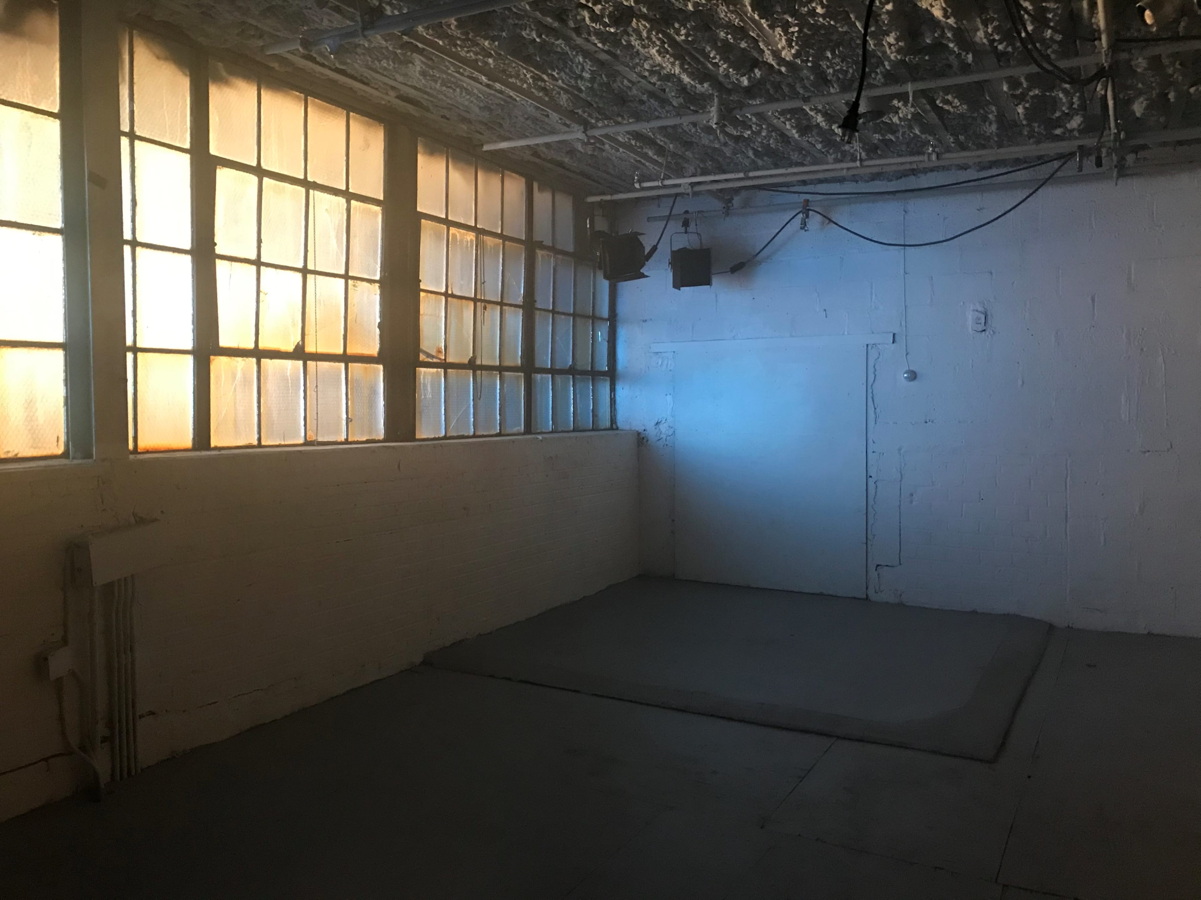 An empty room with large windows letting in orange light, a bare floor, and a single door on one wall.