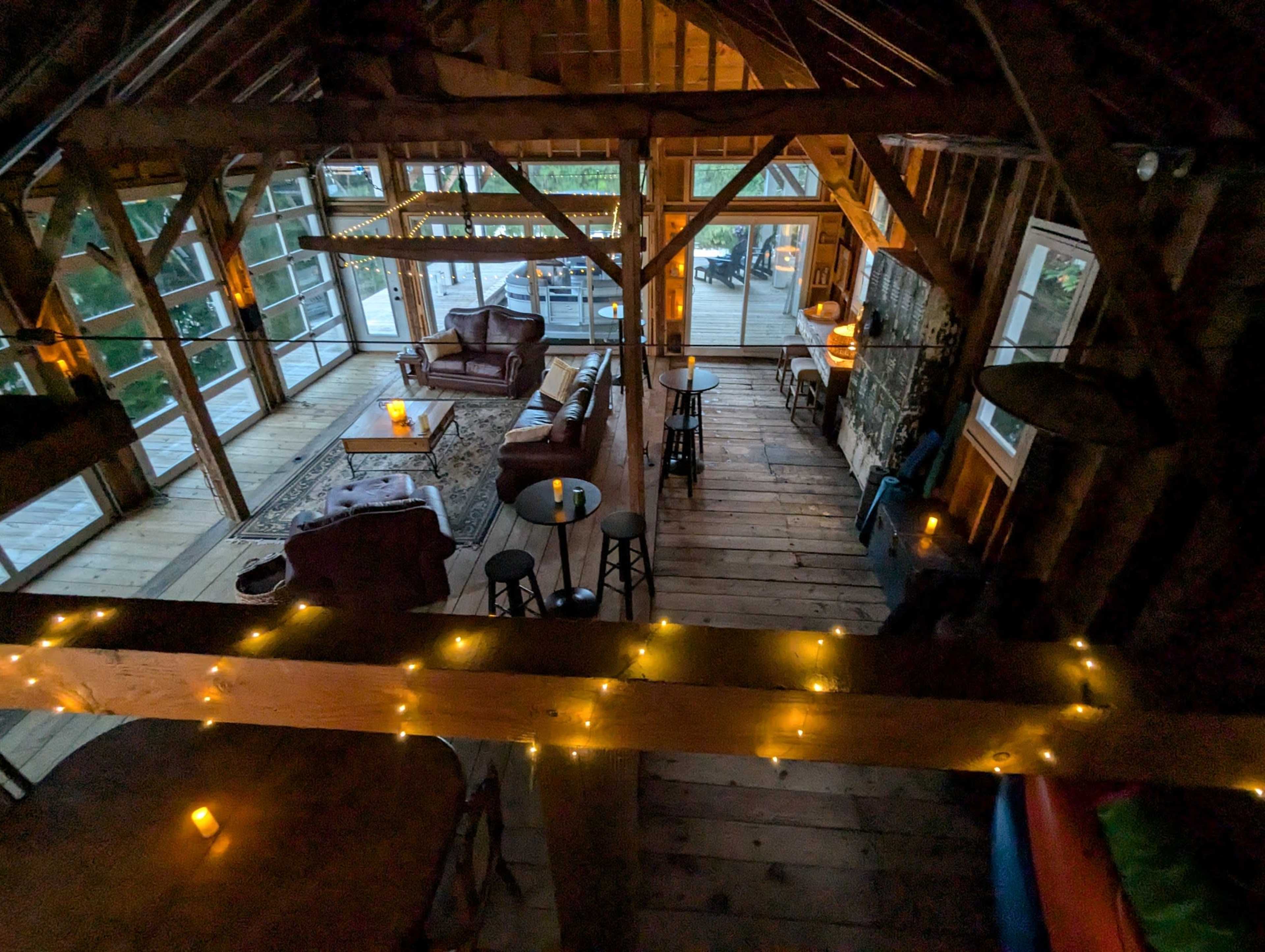 The image shows a rustic wooden cabin interior with large windows, comfortable seating areas, and soft lighting.