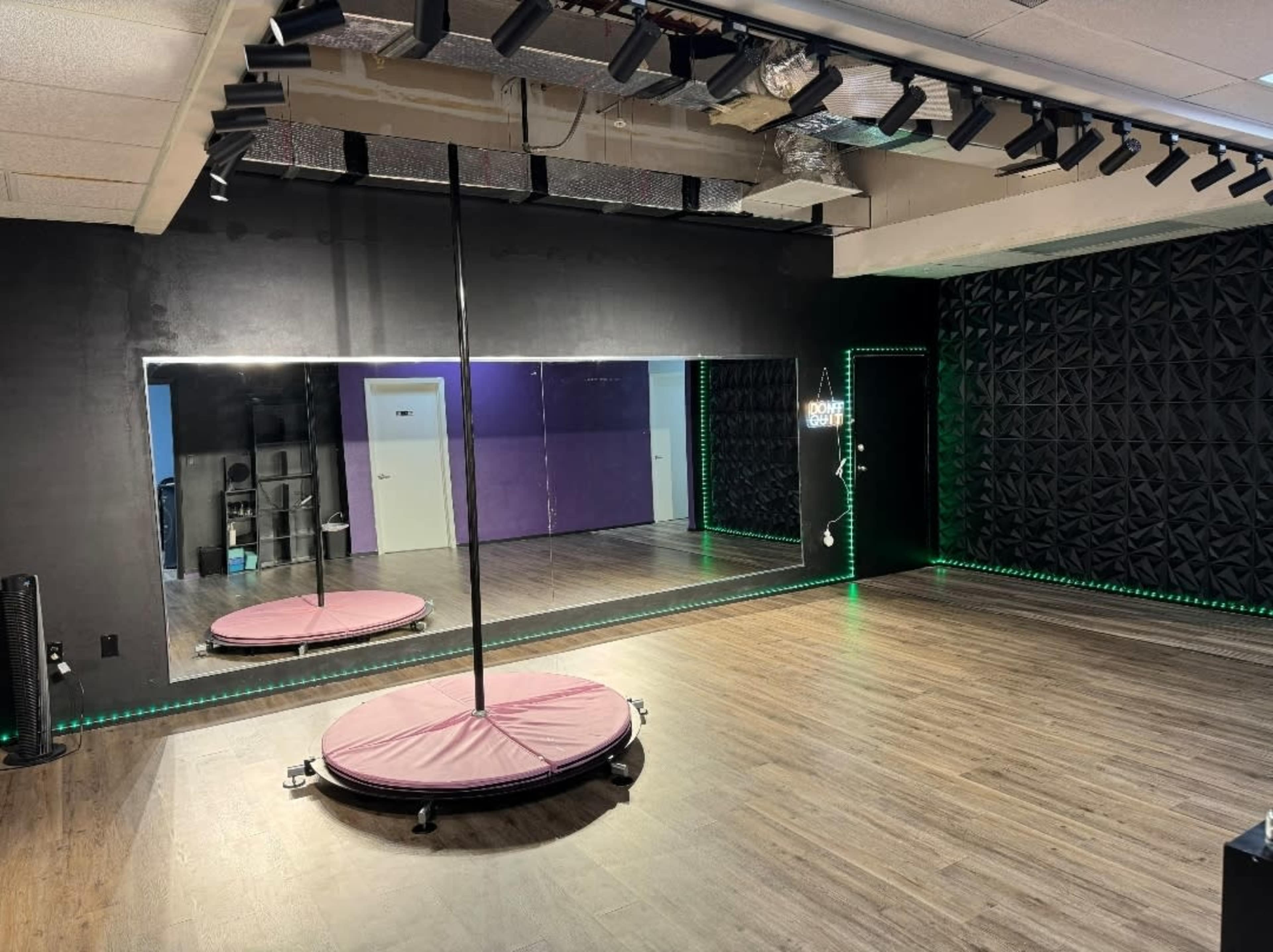 A dance studio featuring a mirrored wall, a central pole, and LED lighting along the edges of the room.