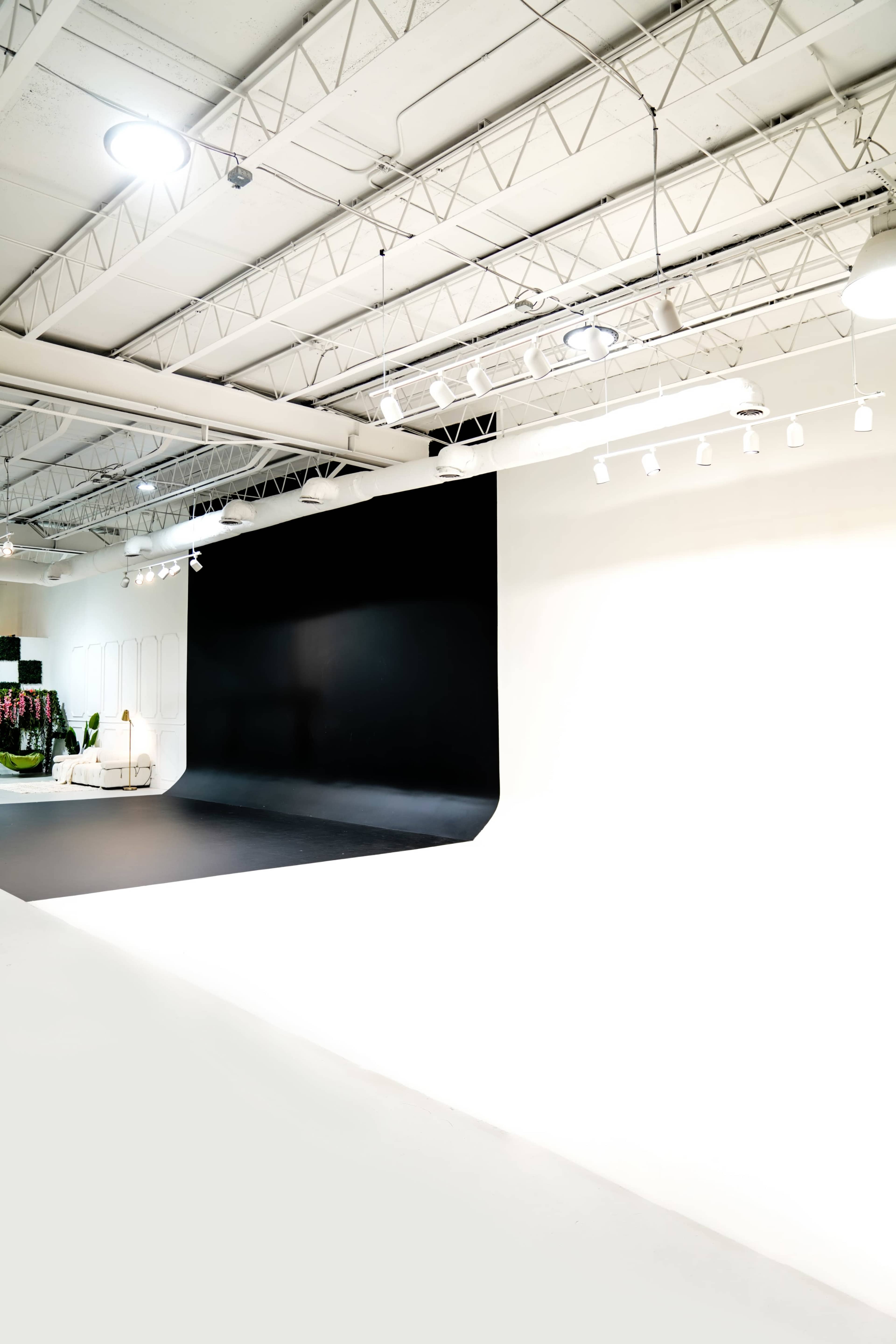 The image shows a spacious studio with a black and white backdrop, bright overhead lighting, and a minimalist design.