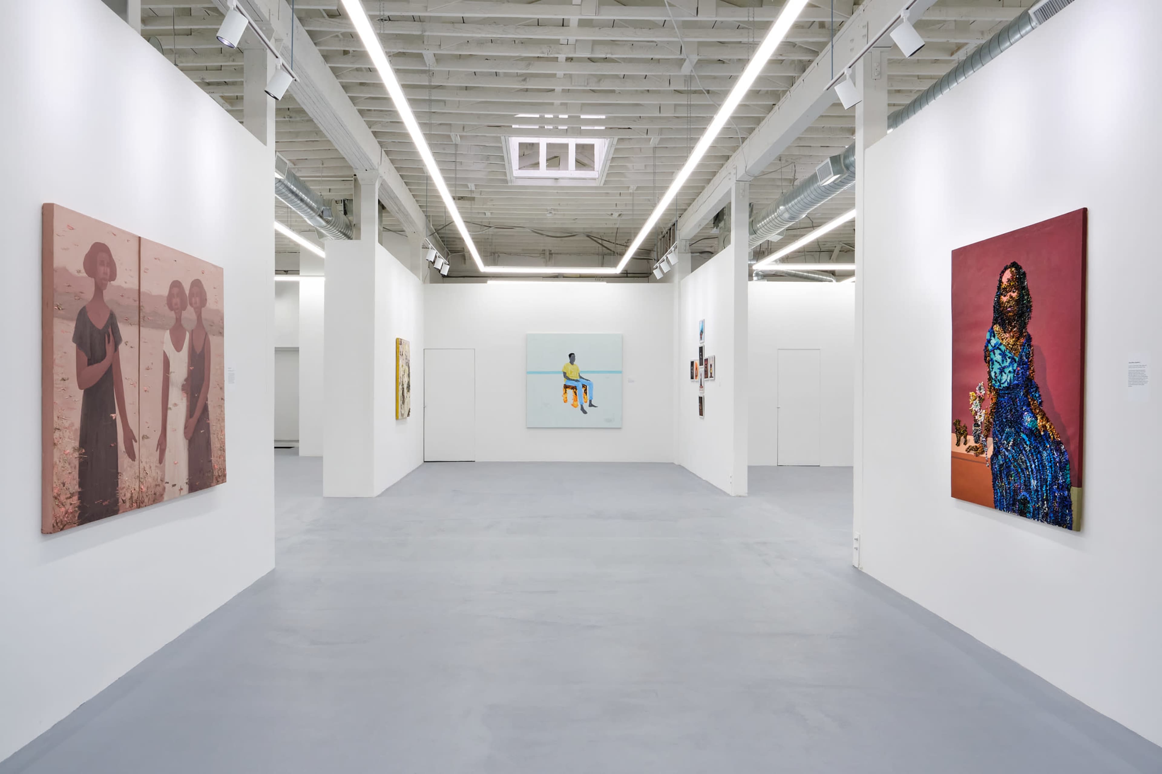 A modern art gallery showcasing several framed artworks on white walls with a gray floor.