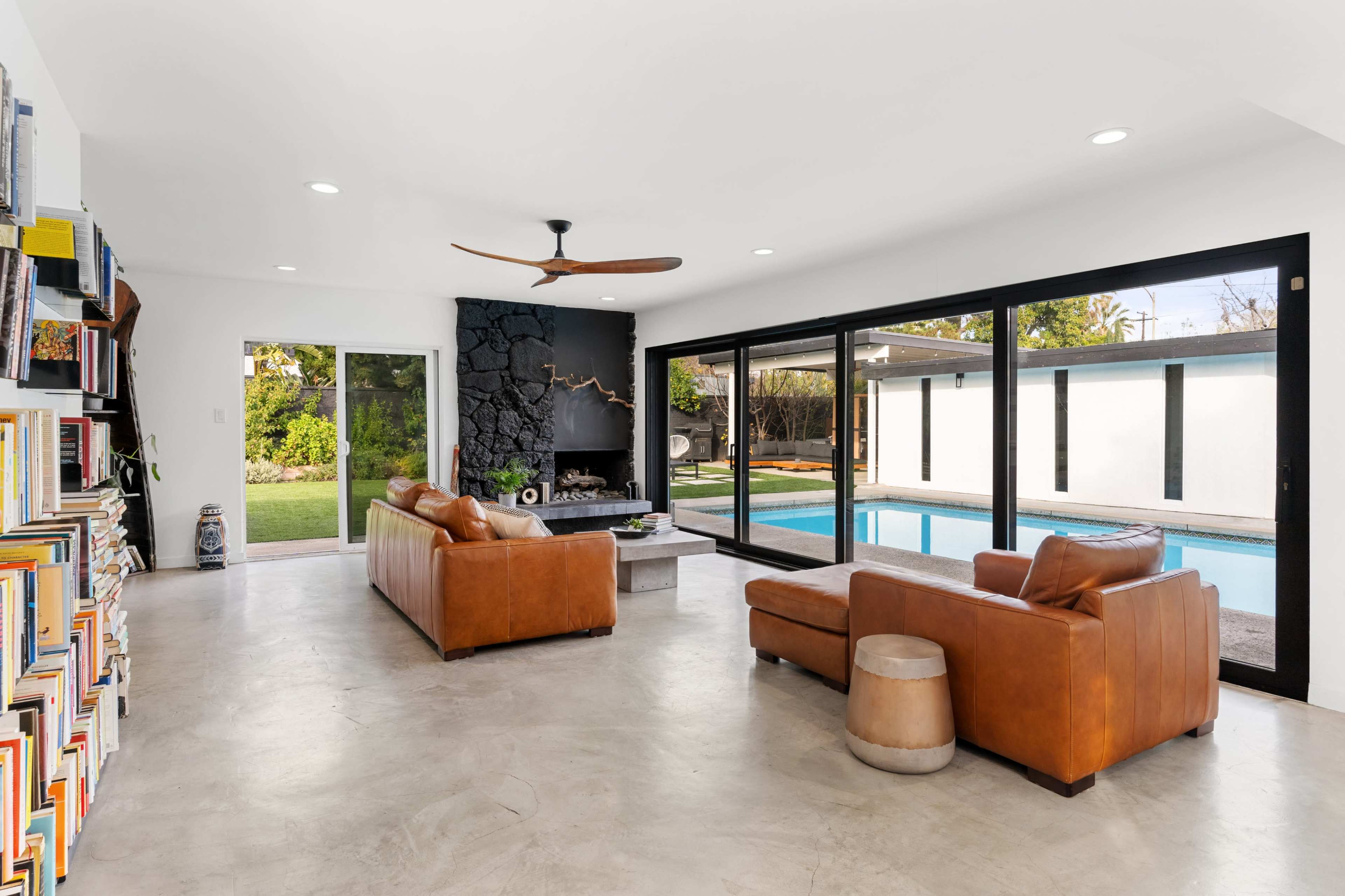 The room features brown leather sofas facing a swimming pool, with large glass doors providing a view of the outdoor area.