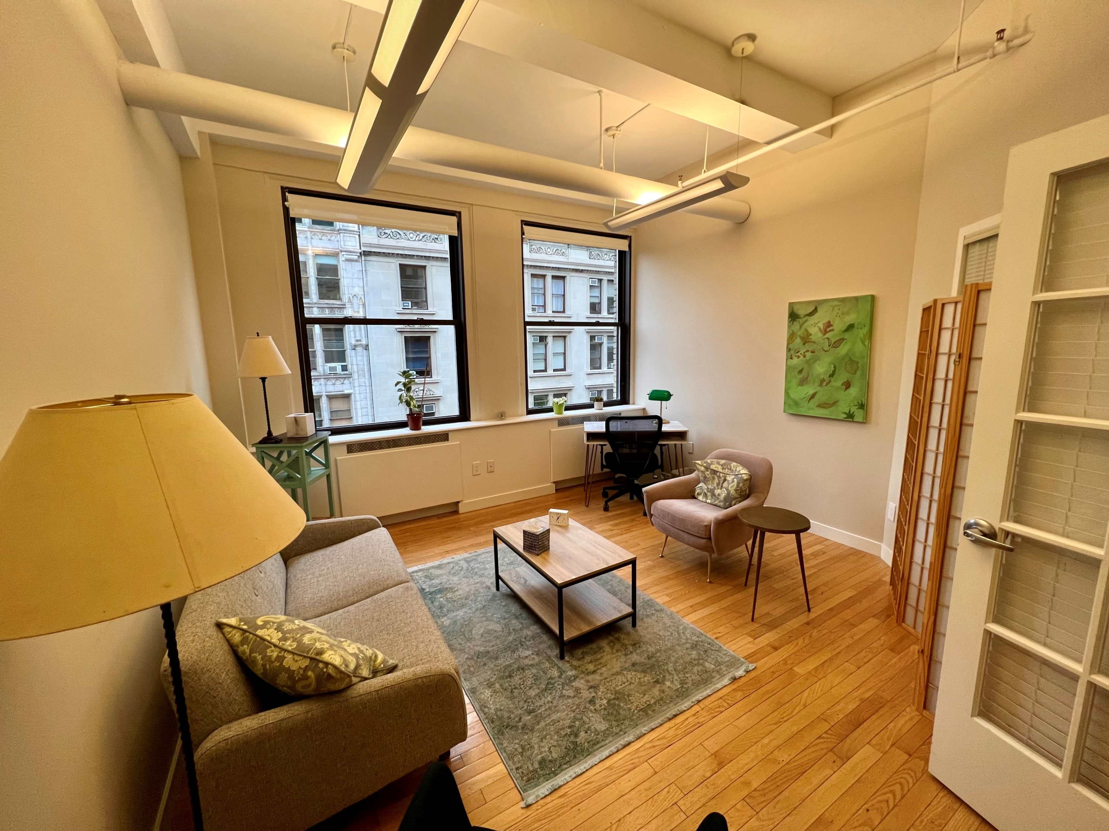 A cozy office space featuring a sofa, two chairs, a coffee table, and large windows that let in natural light.