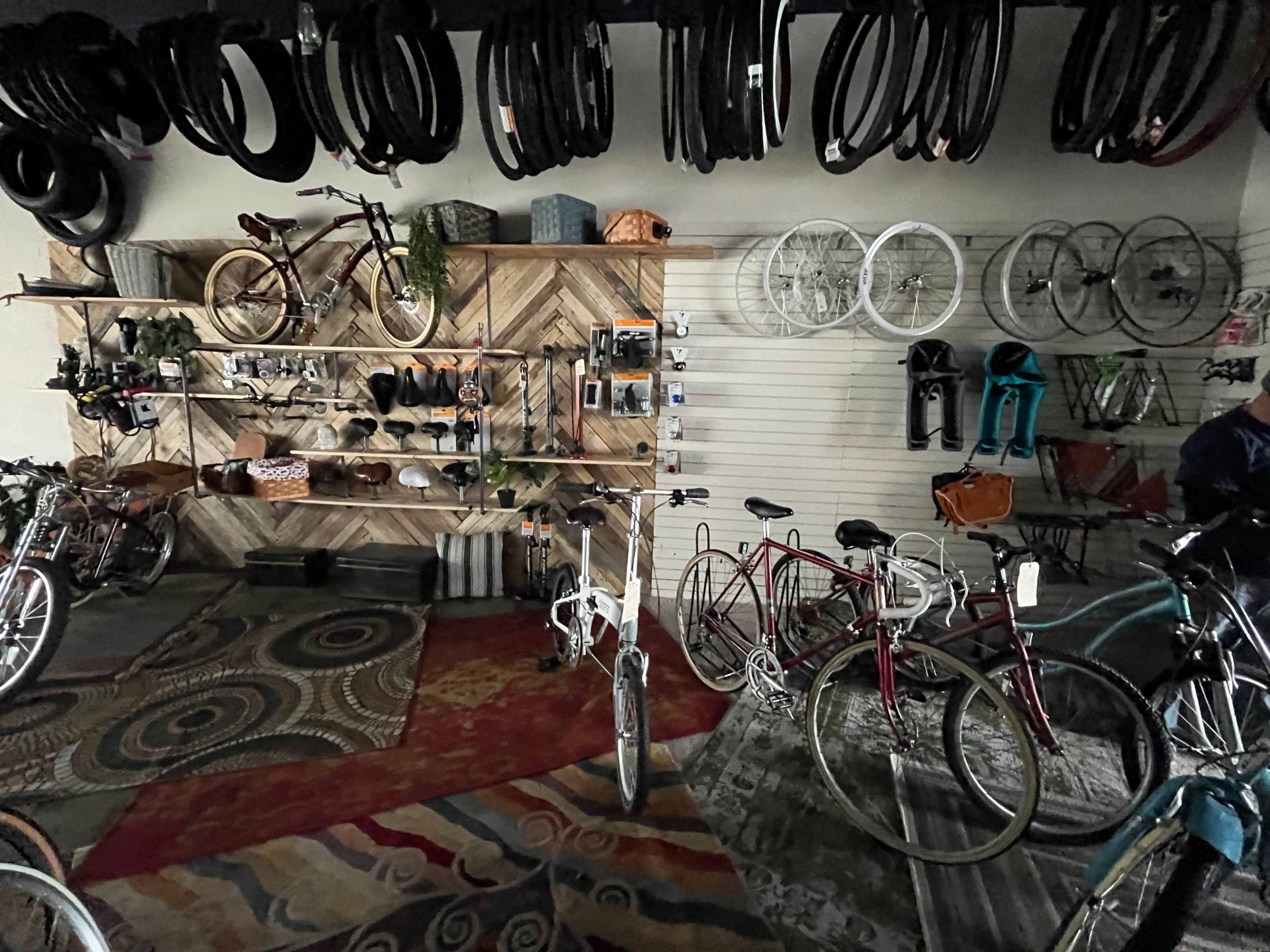 The image shows a bicycle shop interior with various bicycles displayed alongside bike accessories and tires on wall-mounted racks.