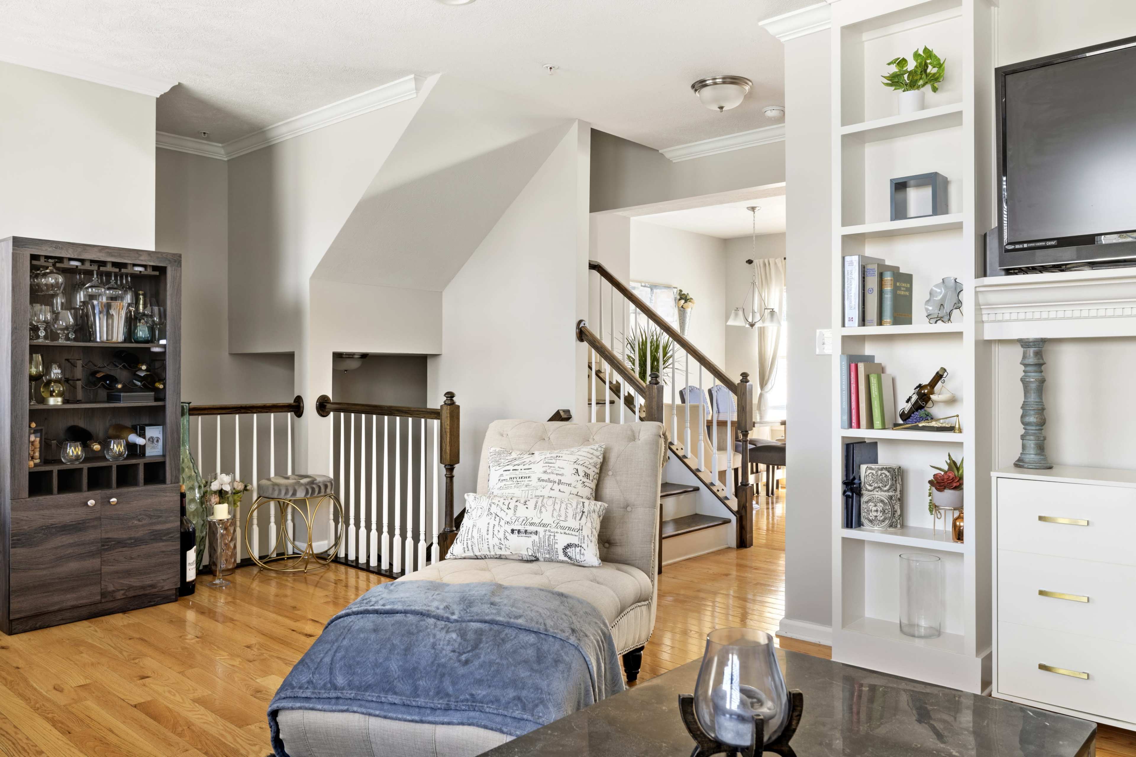 A modern living room featuring a chaise lounge, a bookshelf, and a staircase leading to an upper level.