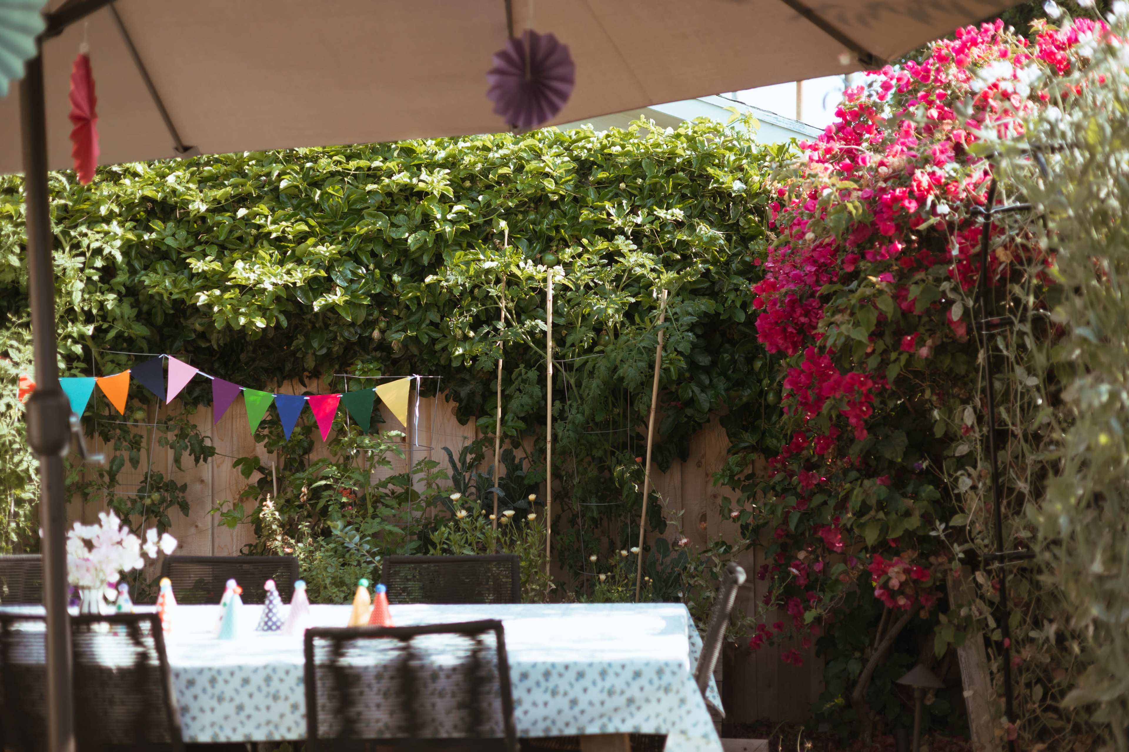 A festive outdoor setting features a table covered with a light blue cloth, surrounded by chairs, adorned with colorful bunting and bordered by vibrant flowers.