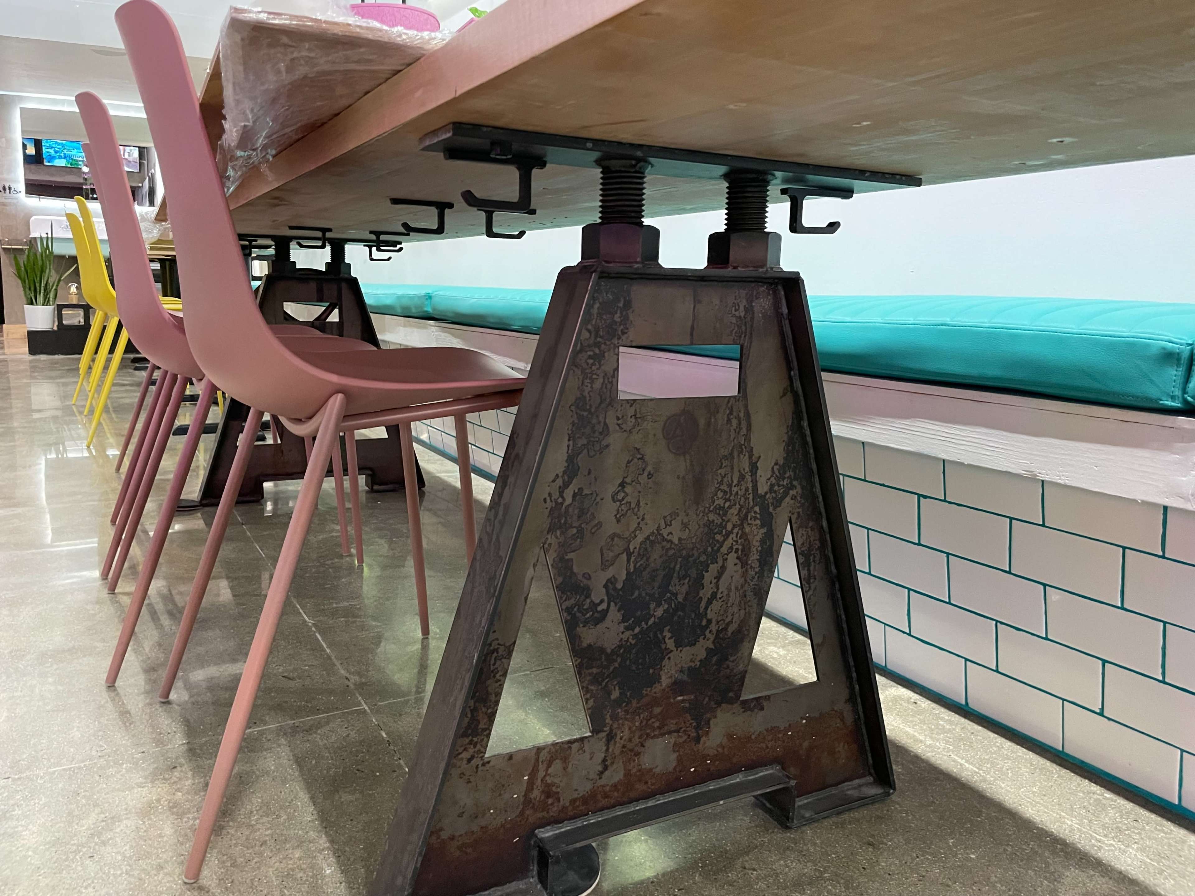 A modern table supported by a metal base with adjustable clamps, accompanied by colorful chairs arranged around it.
