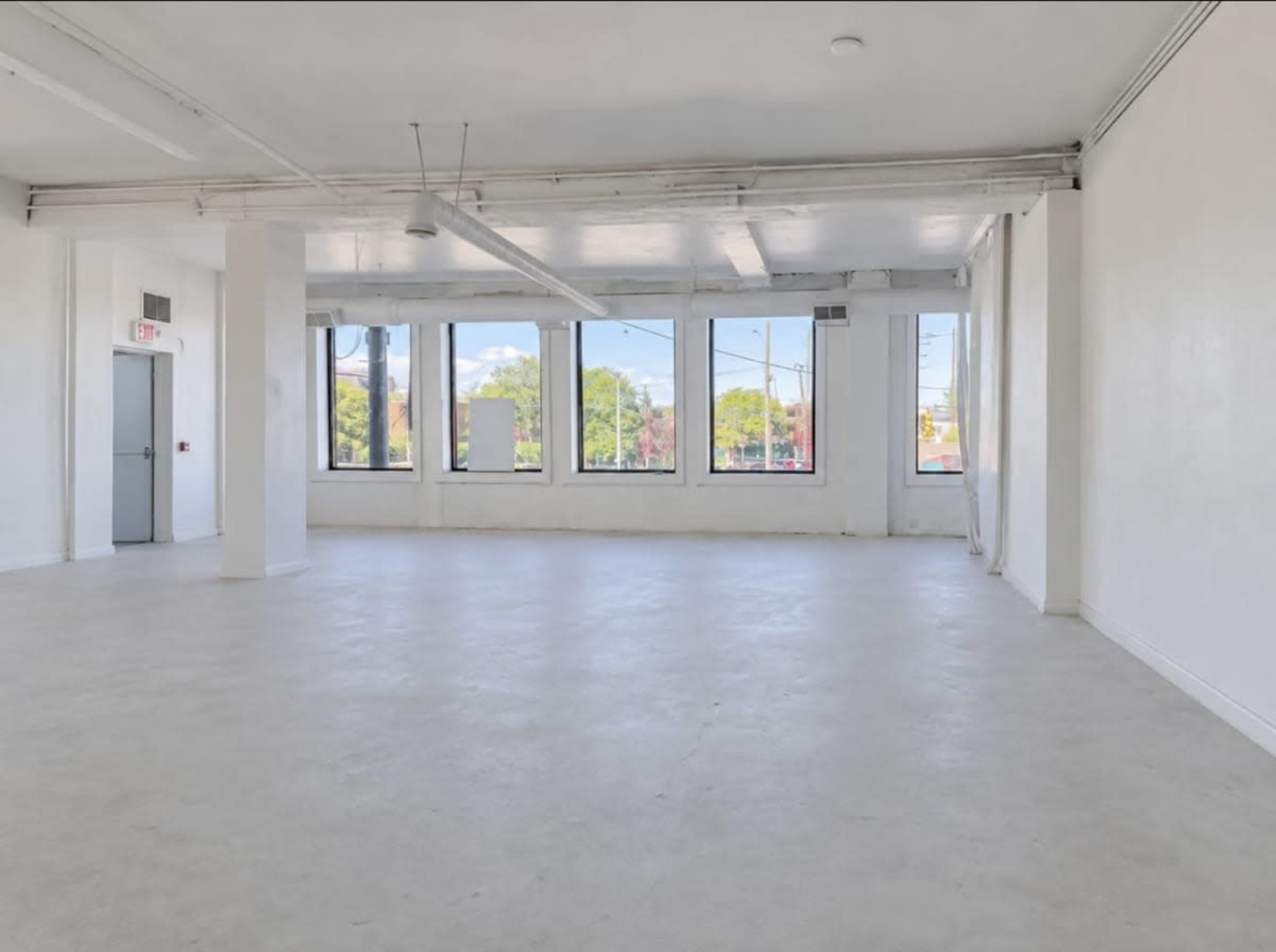 A spacious, empty room with white walls and a polished concrete floor features large windows that let in natural light.