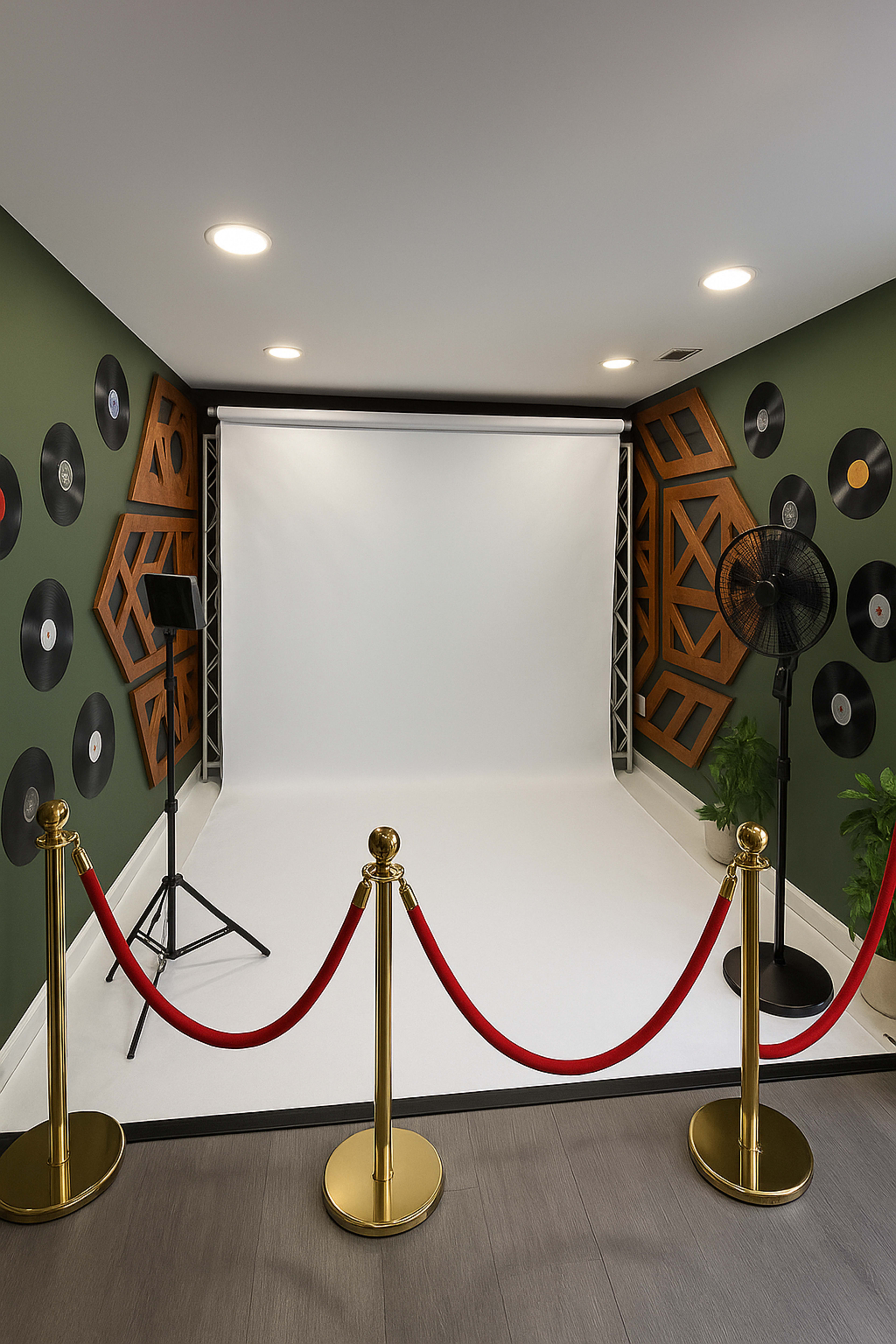 A photo studio features a white backdrop with a spotlight, surrounded by black vinyl records on the walls and red velvet ropes at the entrance.