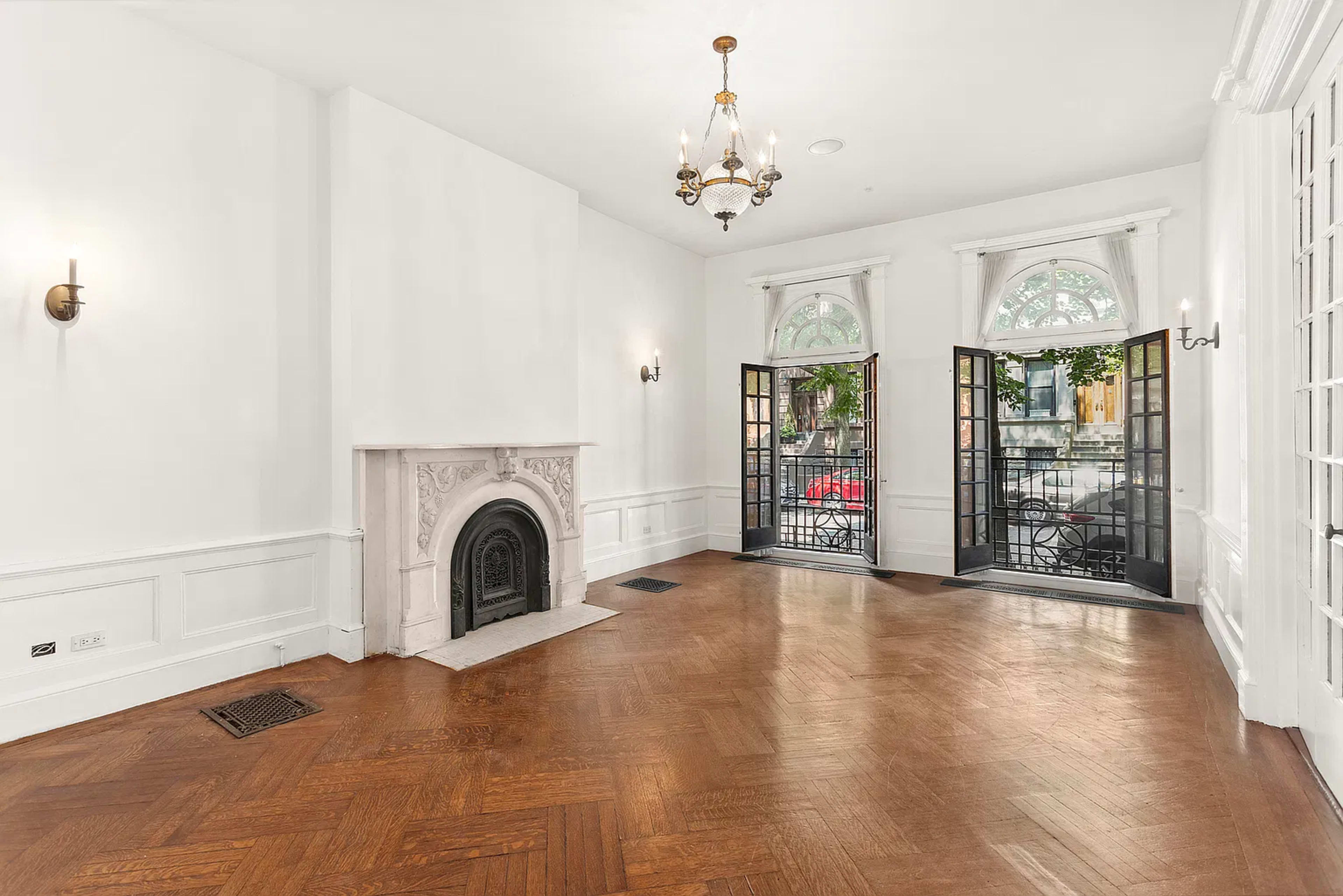 The image depicts a spacious, empty room featuring a decorative fireplace and large, open windows that lead to an outdoor area.