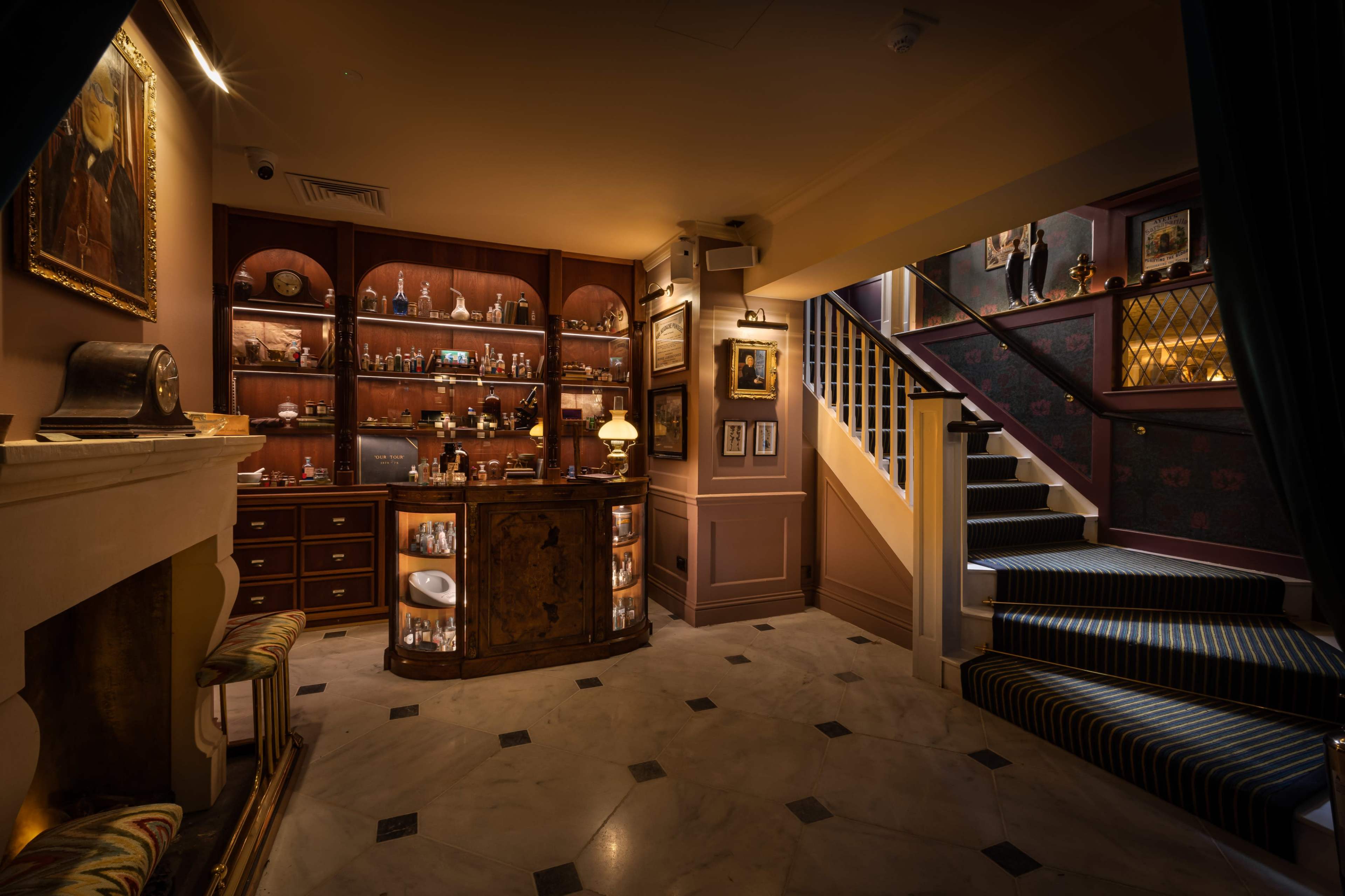 A well-appointed bar area with a wooden counter, shelves filled with various bottles, and a staircase leading to an upper level.