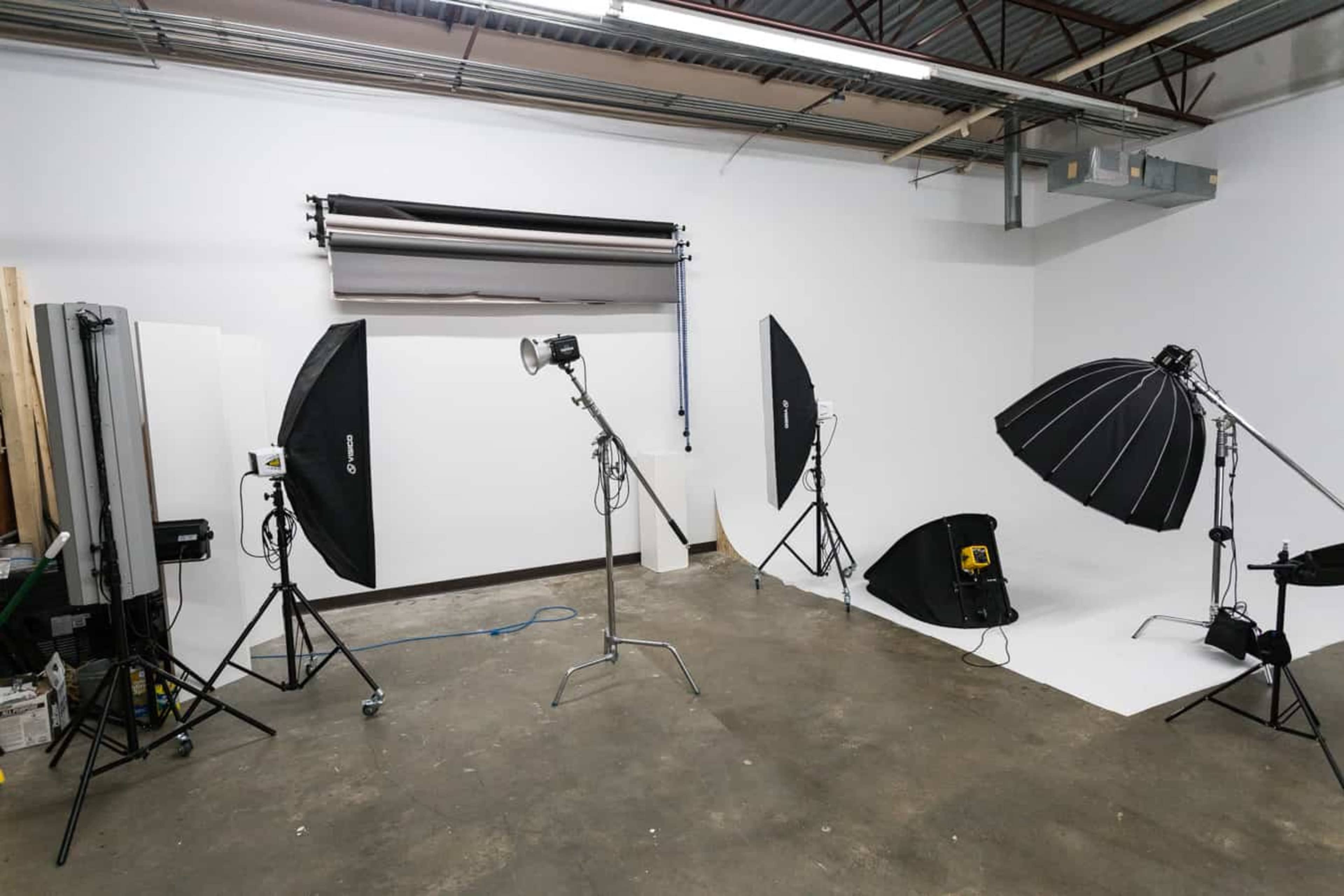 A photography studio is set up with various lighting equipment and backdrops against a white wall.