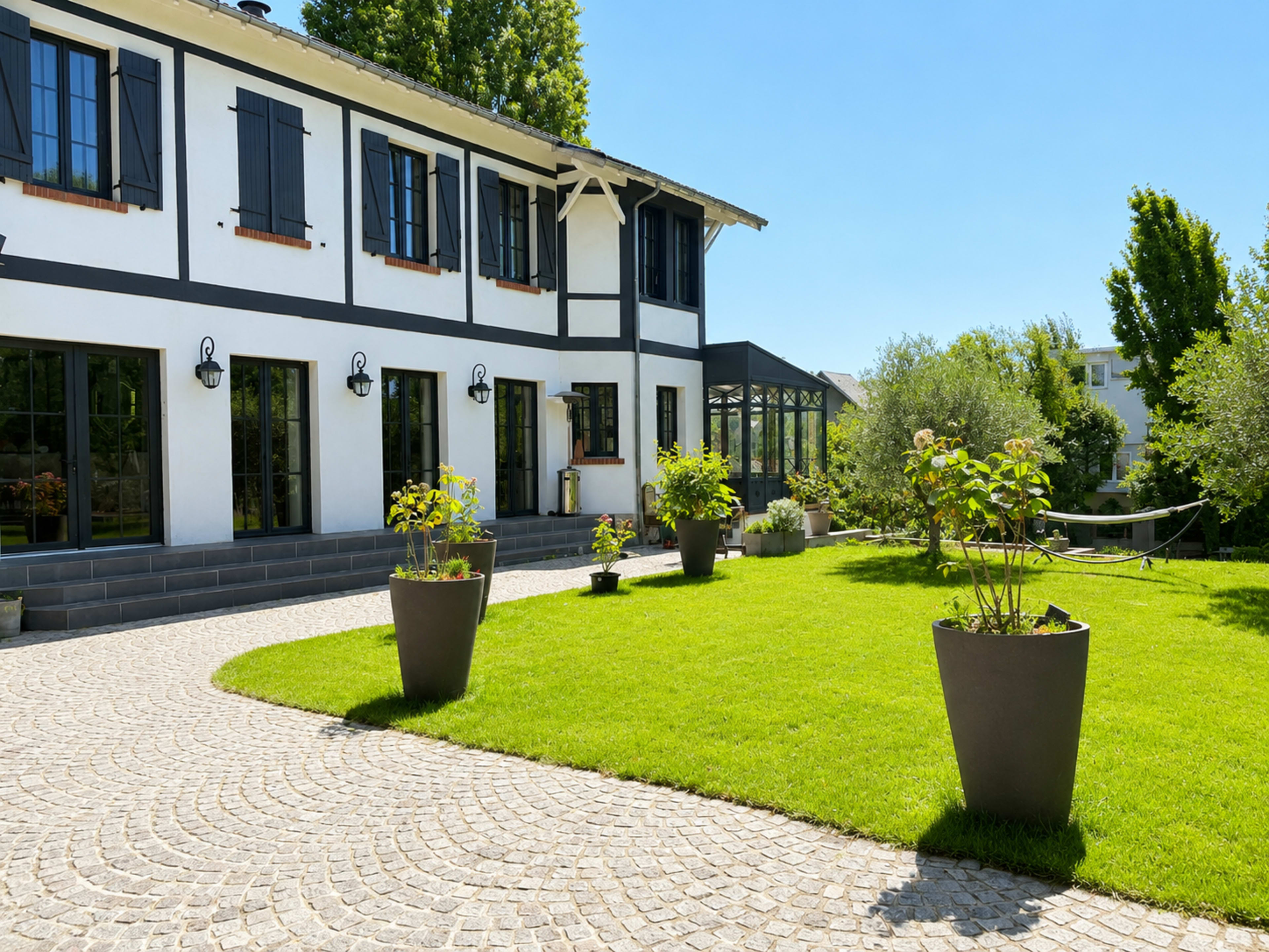 A modern house with large windows and black shutters is set in a landscaped yard featuring a stone pathway and potted plants.