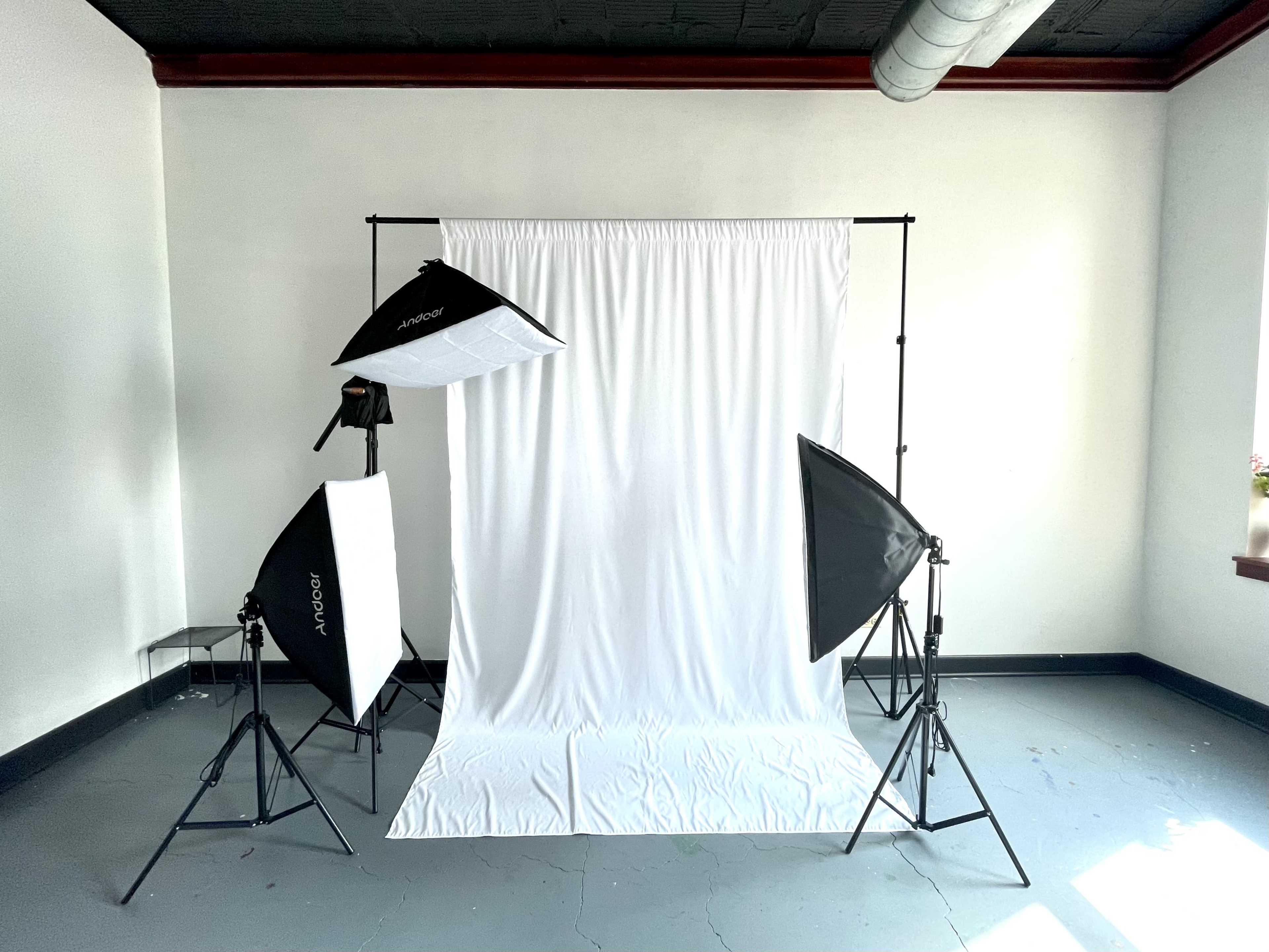 A photography studio setup with a white backdrop and three lighting softboxes positioned around it.