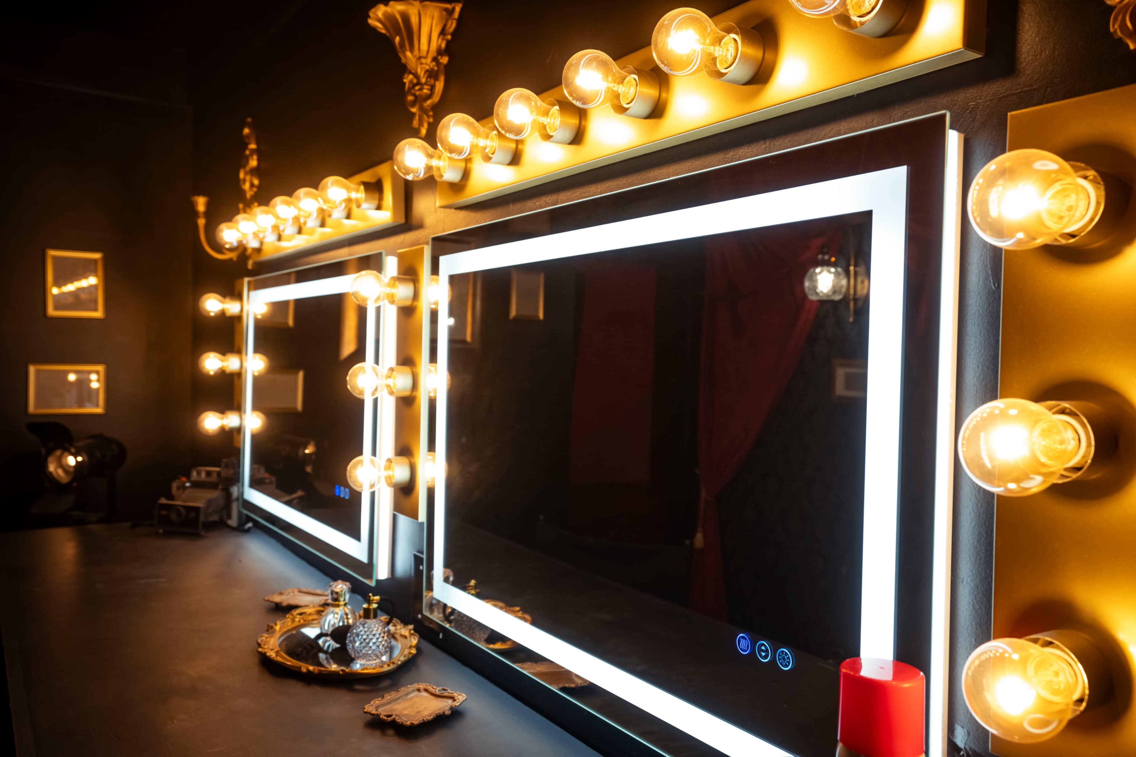 A dimly lit dressing room with two illuminated mirrors framed by bright light bulbs.