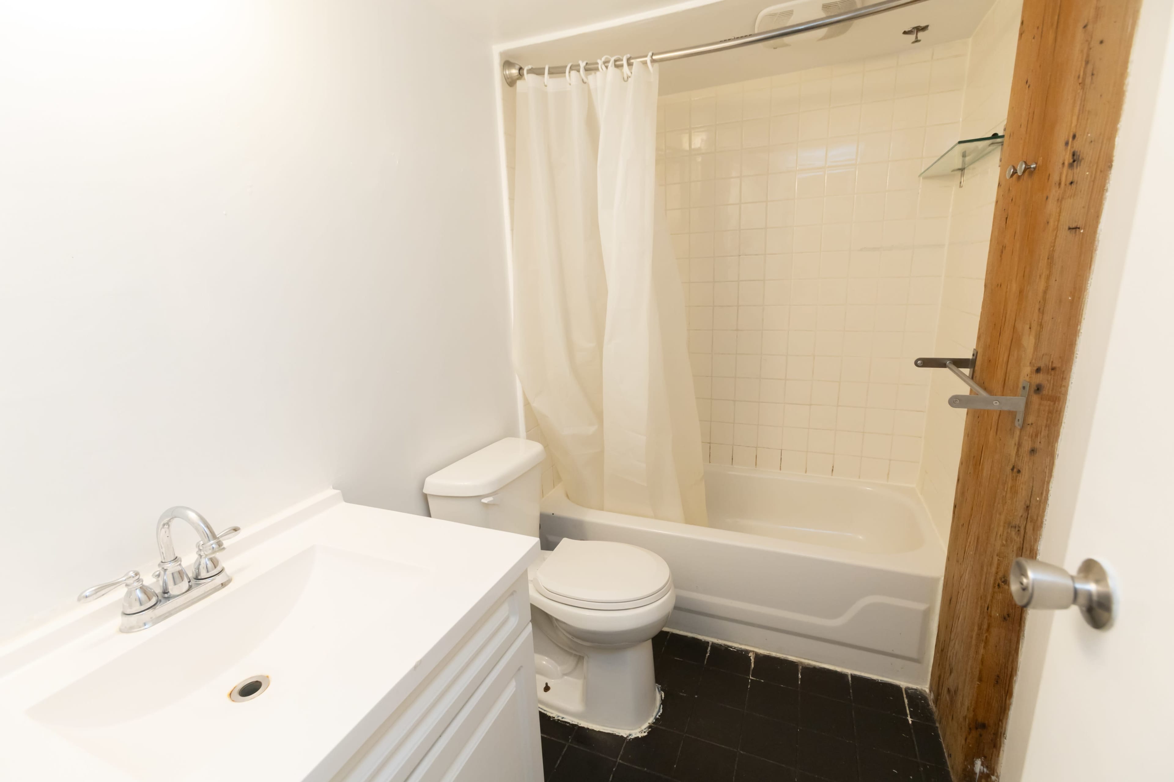 The image shows a small bathroom with a white bathtub and shower, a toilet, and a sink with a cabinet.