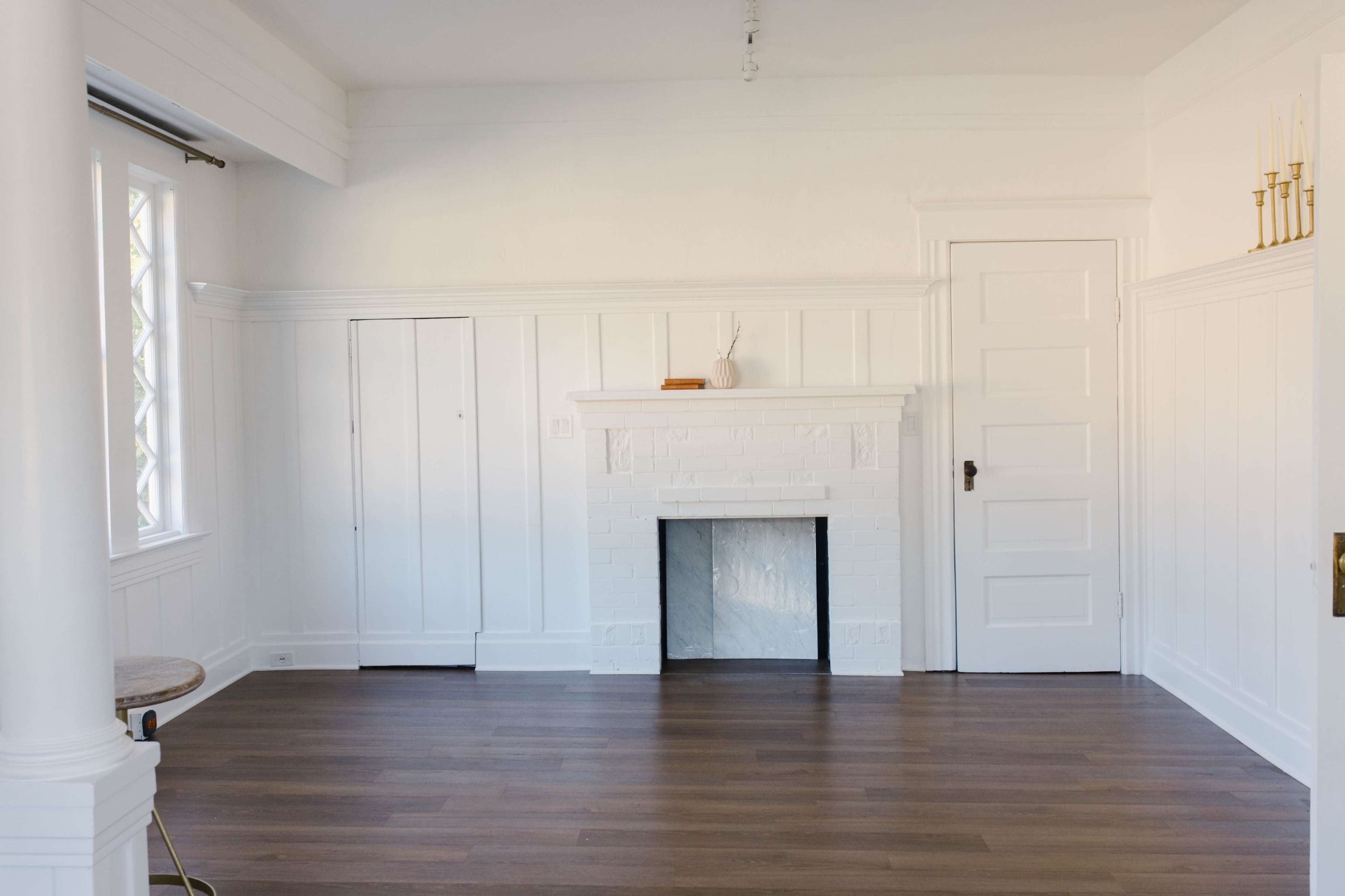 A bright, empty room with white walls, a brick fireplace, and wooden flooring.