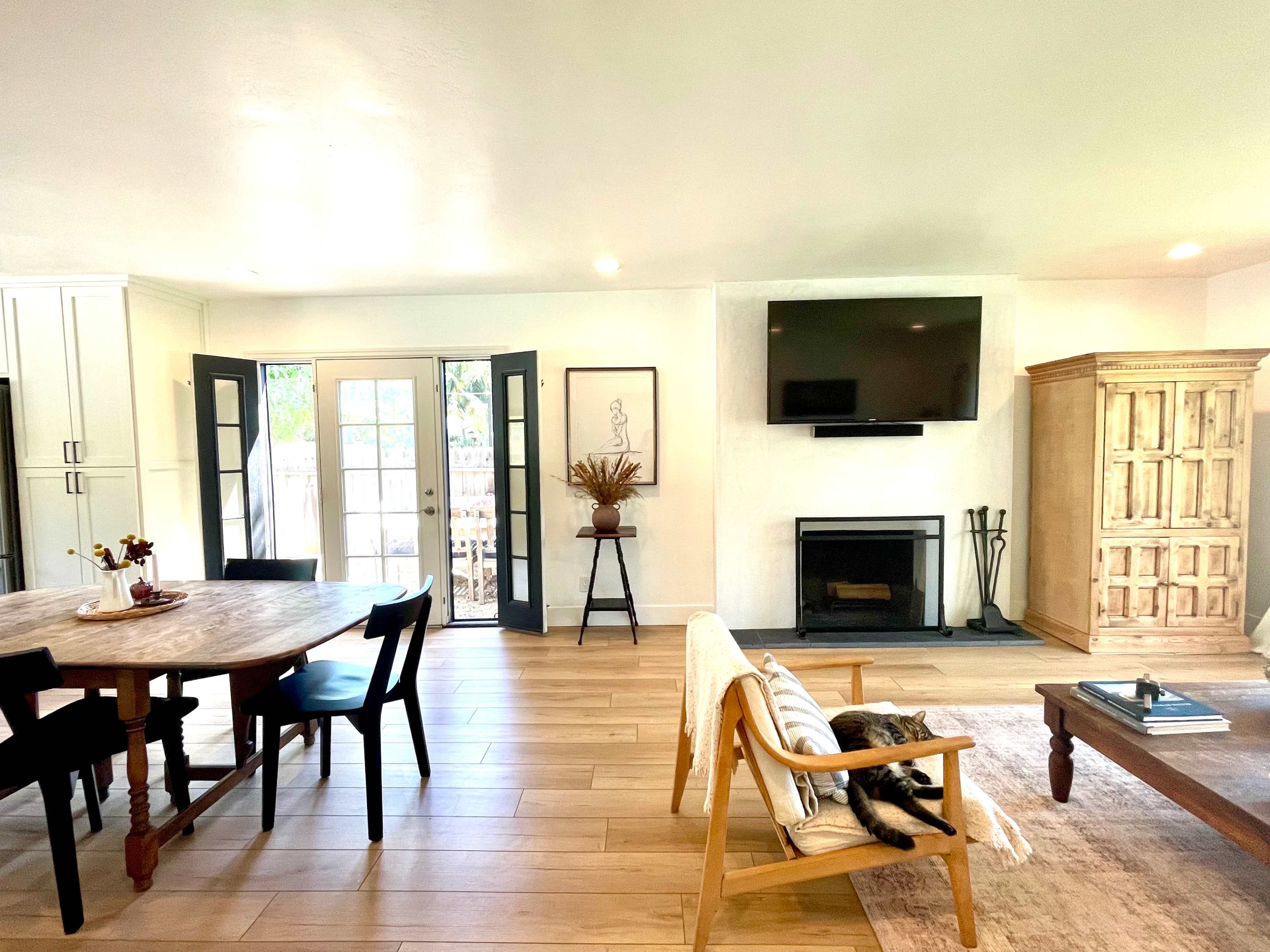 A modern living space featuring a dining area with a round table, a cozy sitting area with a fireplace, and large windows leading to an outdoor space.