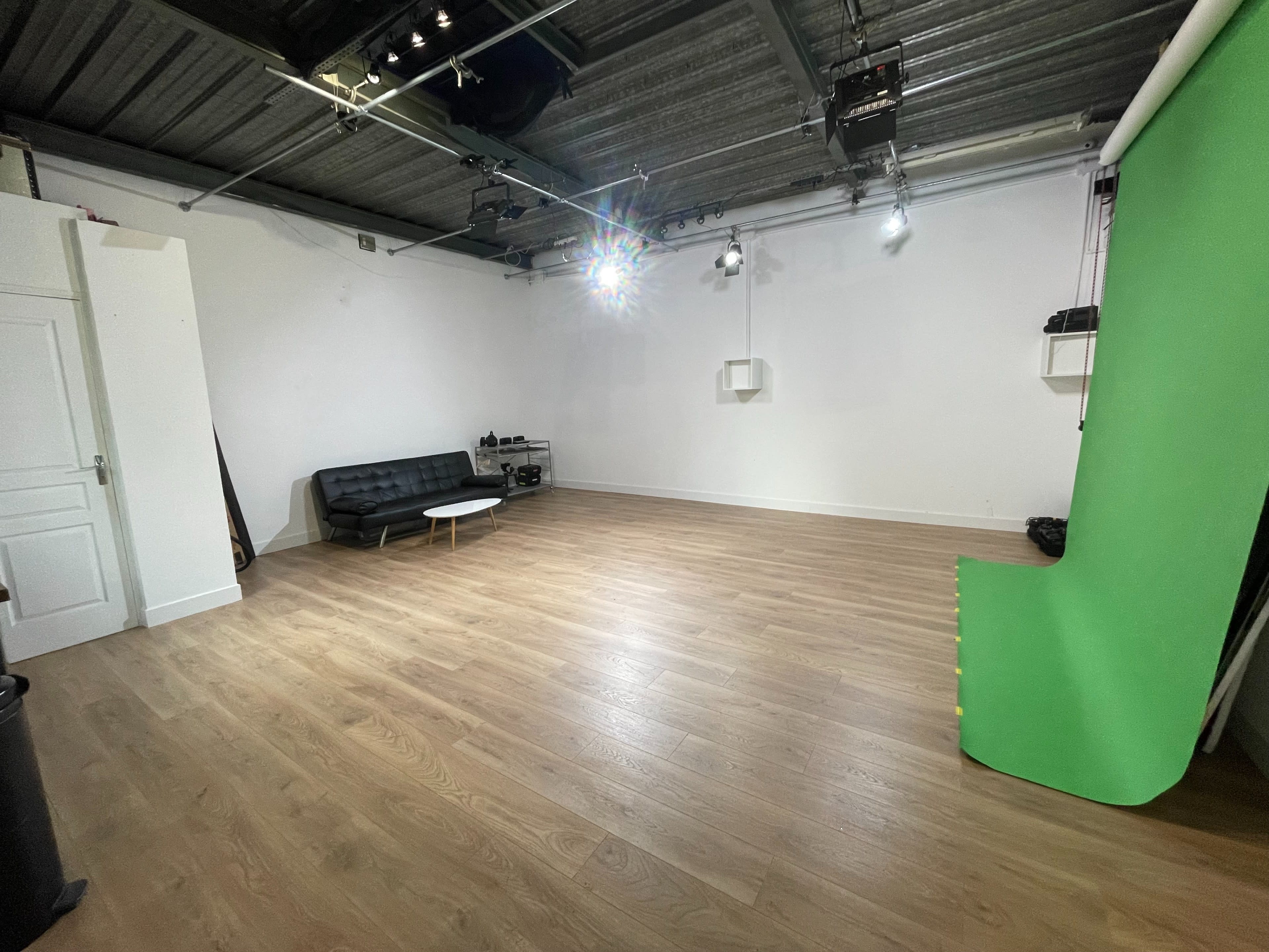 An empty photo studio featuring a black sofa, a small white coffee table, and a green backdrop along one wall.