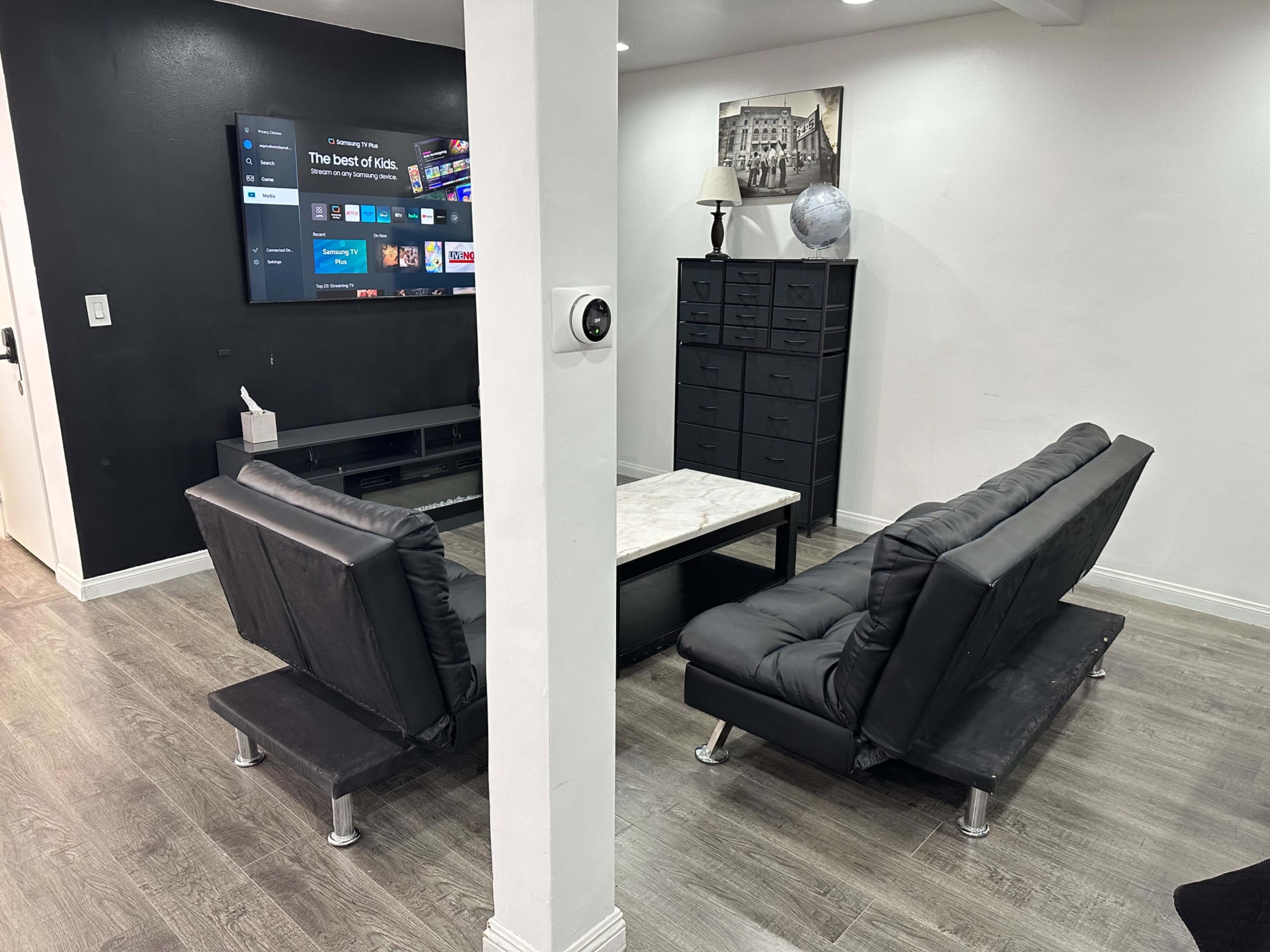 The image shows a modern living room with two black couches facing a television mounted on a wall and a marble-topped coffee table in between.