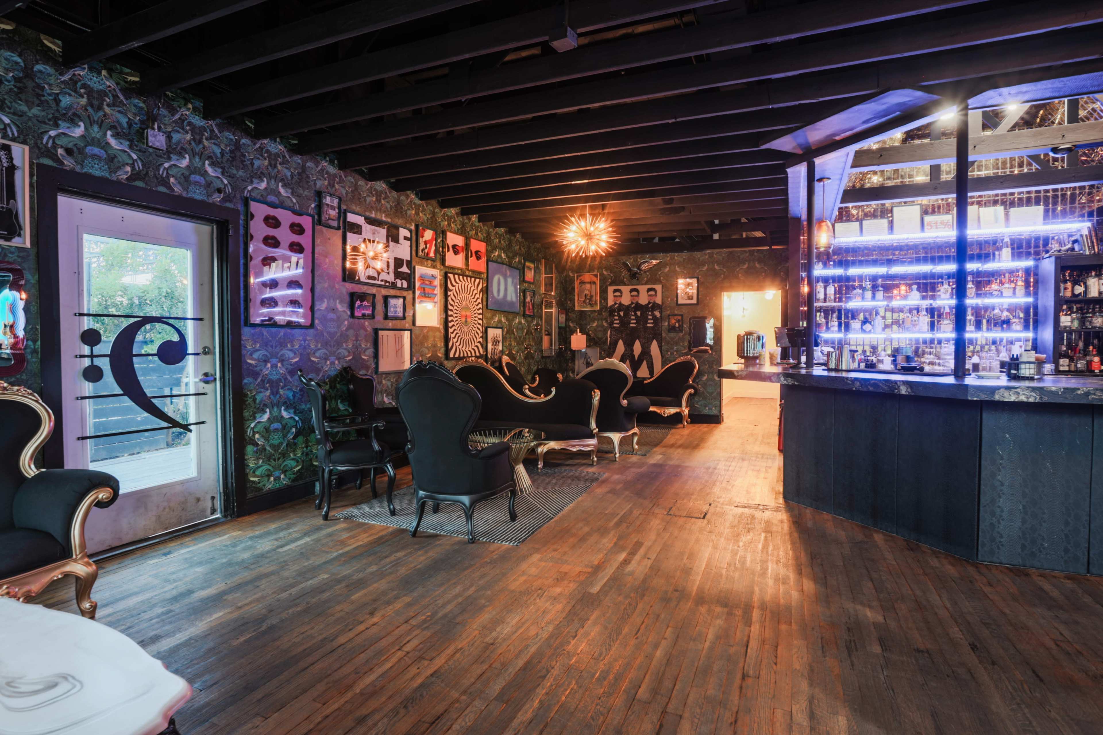 A stylish bar area with dark wood flooring, vintage seating, and a well-lit bar featuring a variety of bottles.
