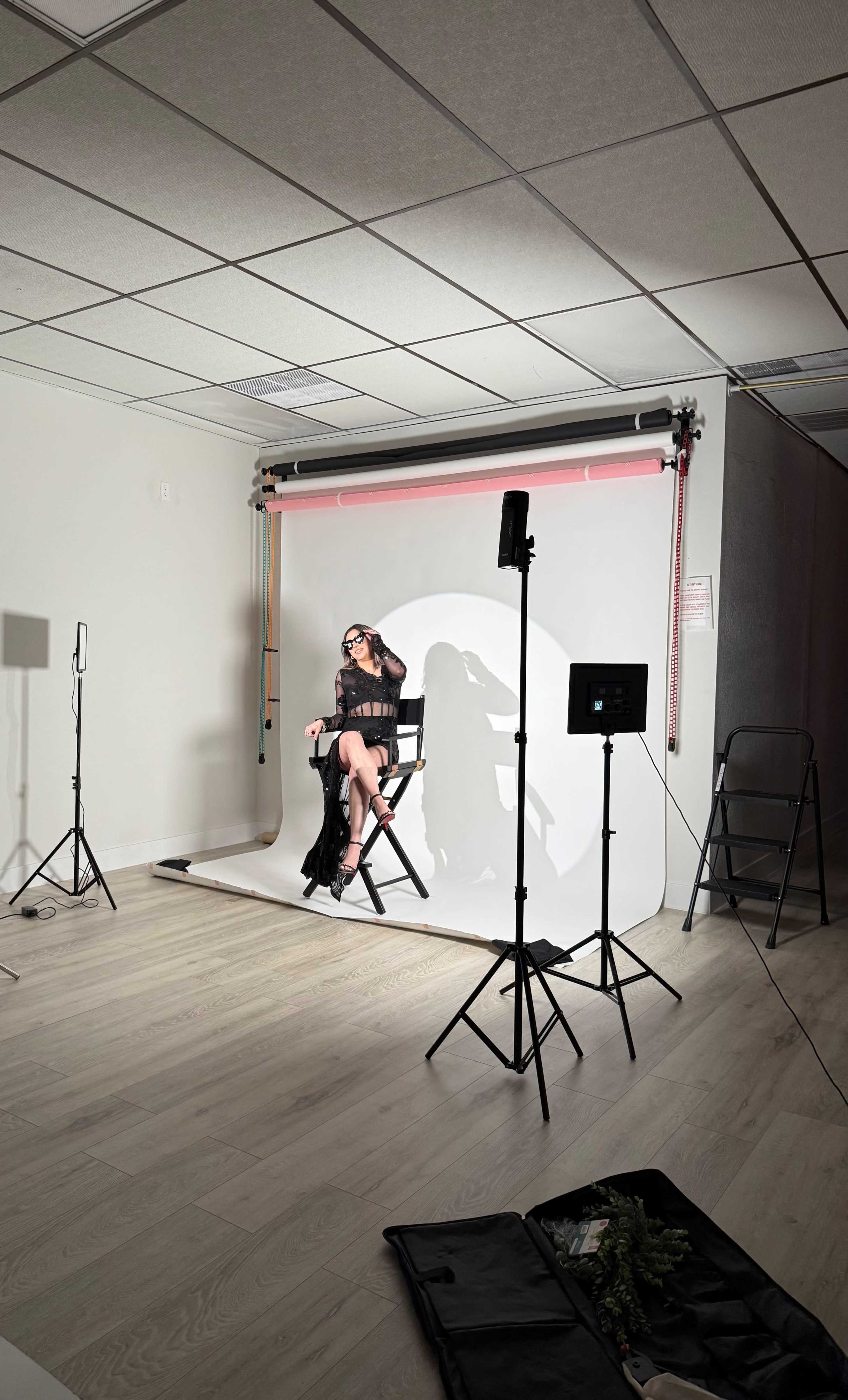 A person sits on a director's chair in front of a blank backdrop in a well-lit studio.