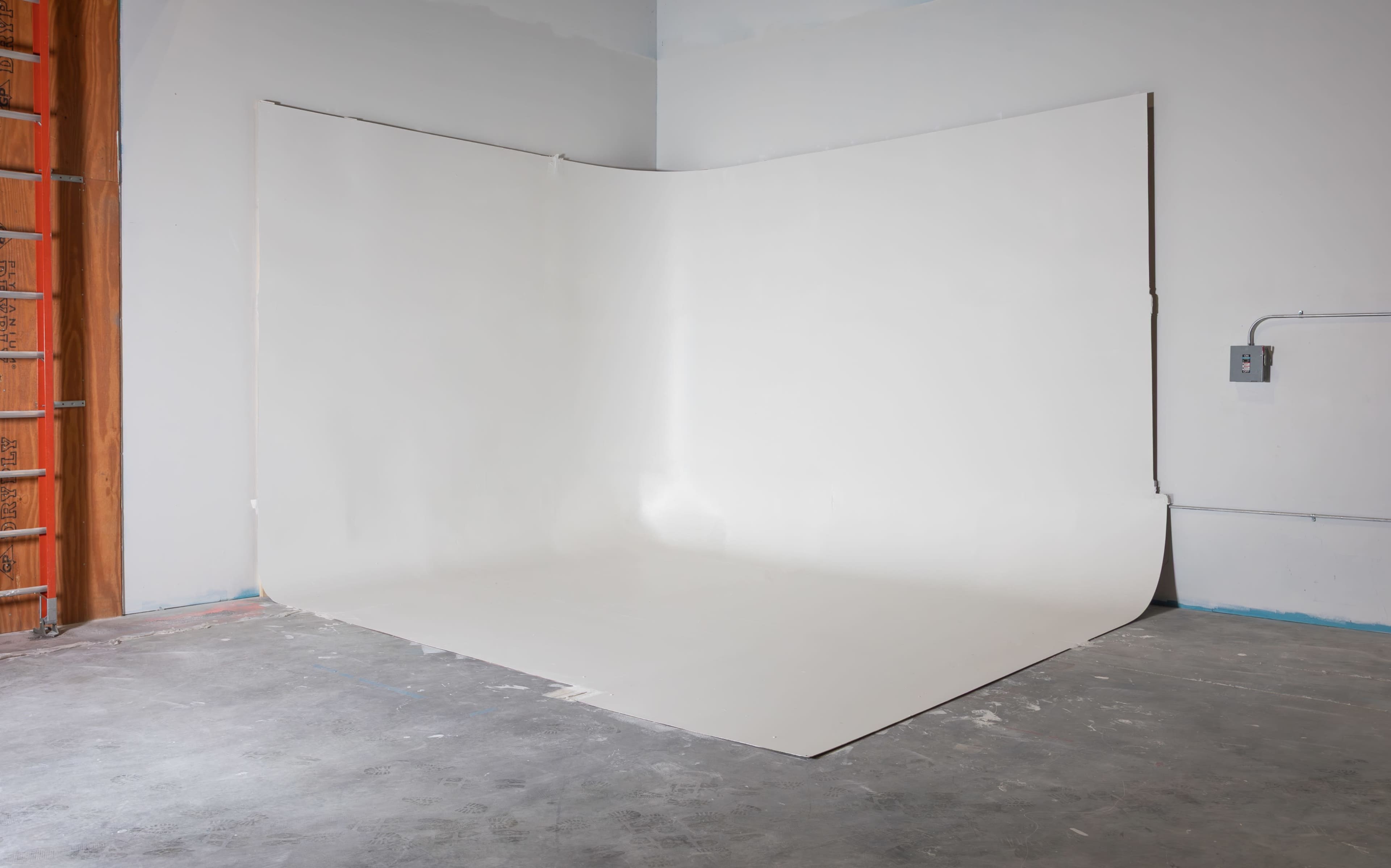 The image shows a minimalist photo studio setup with a seamless white backdrop against a gray concrete floor.