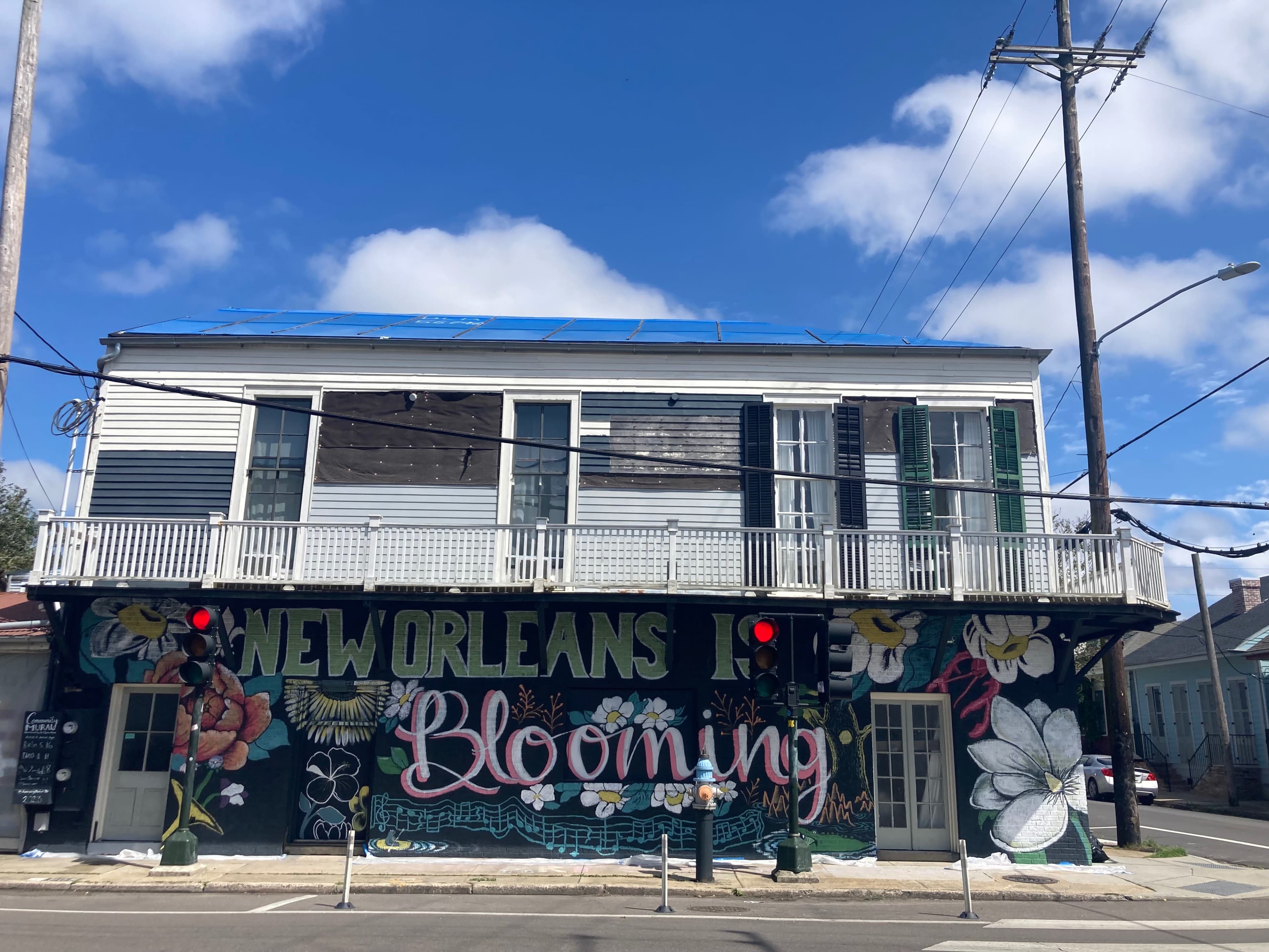 The image shows a two-story building in New Orleans featuring a colorful mural on its lower level that reads "Blooming" alongside floral designs.