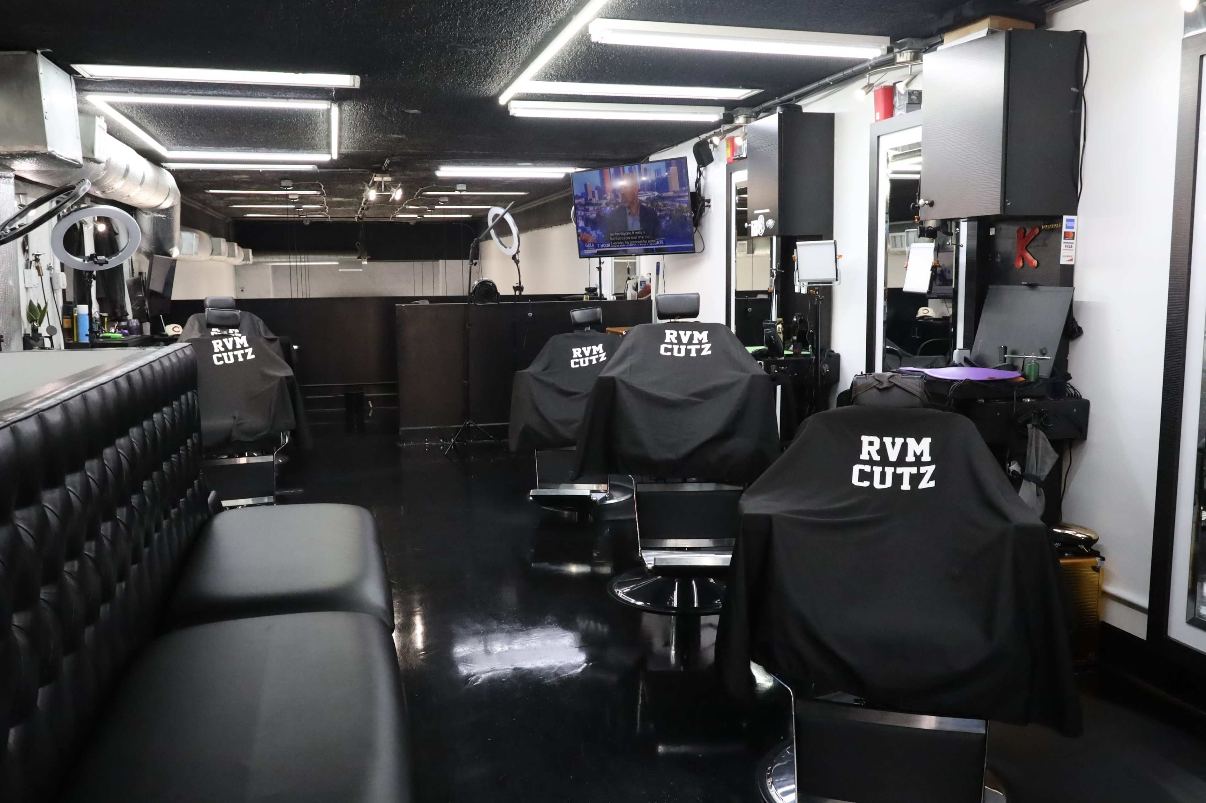 An interior of a modern barbershop with black leather seating and several barber stations equipped with mirrors and chairs.