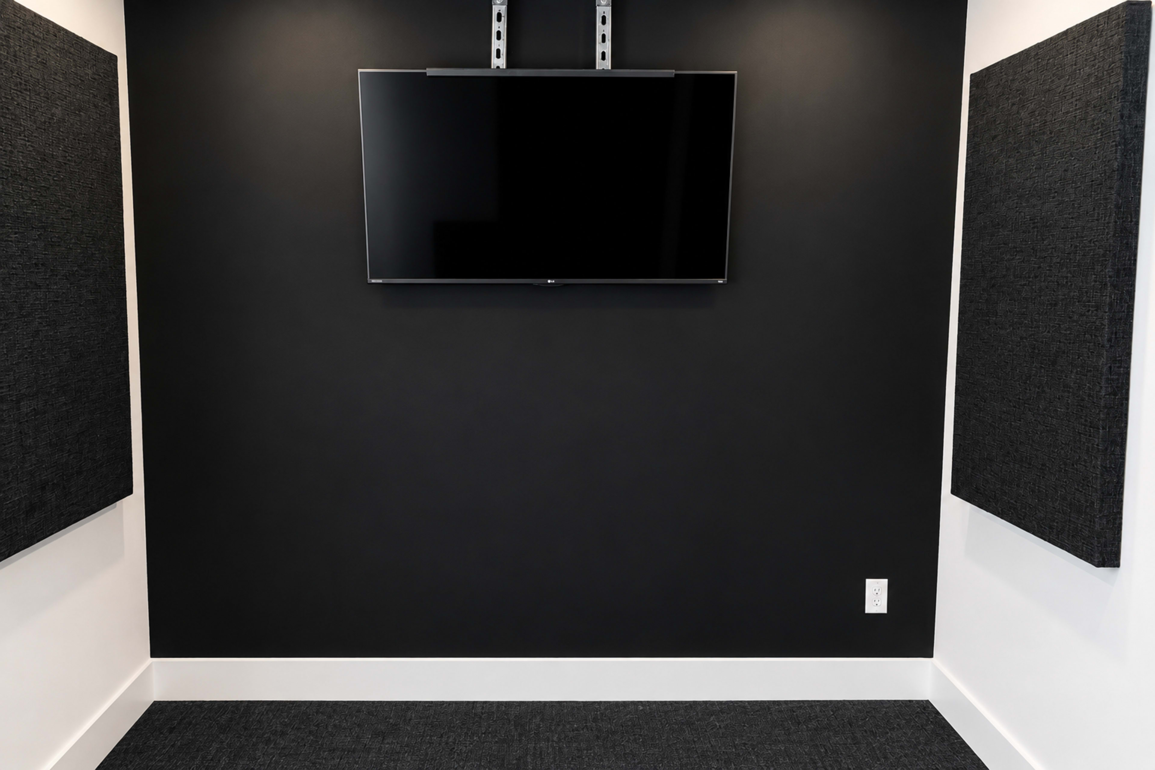 The image shows a minimalistic room with a black wall, a mounted television screen, and acoustic panels flanking the sides.