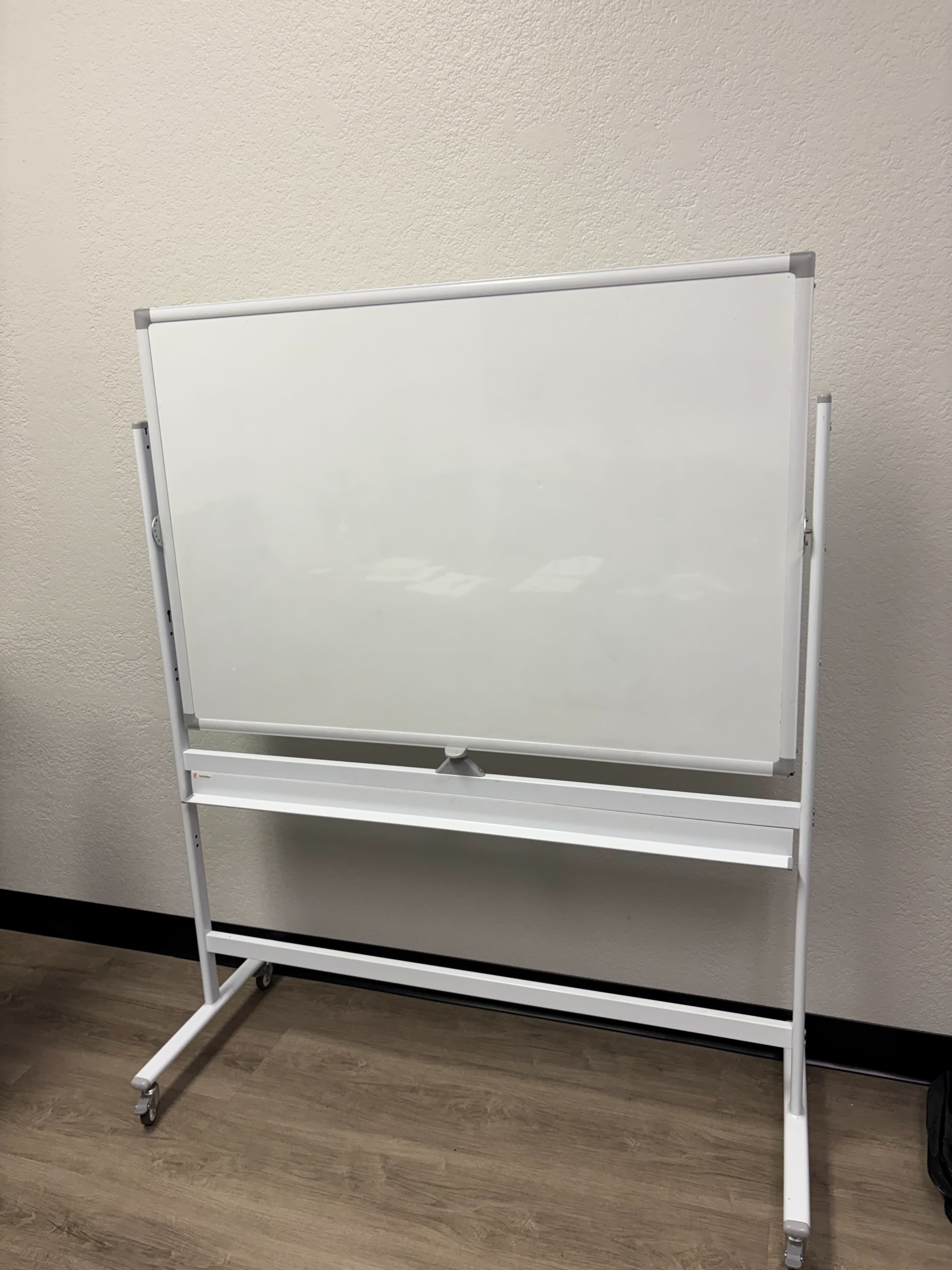 A whiteboard on a mobile stand is positioned against a plain wall.