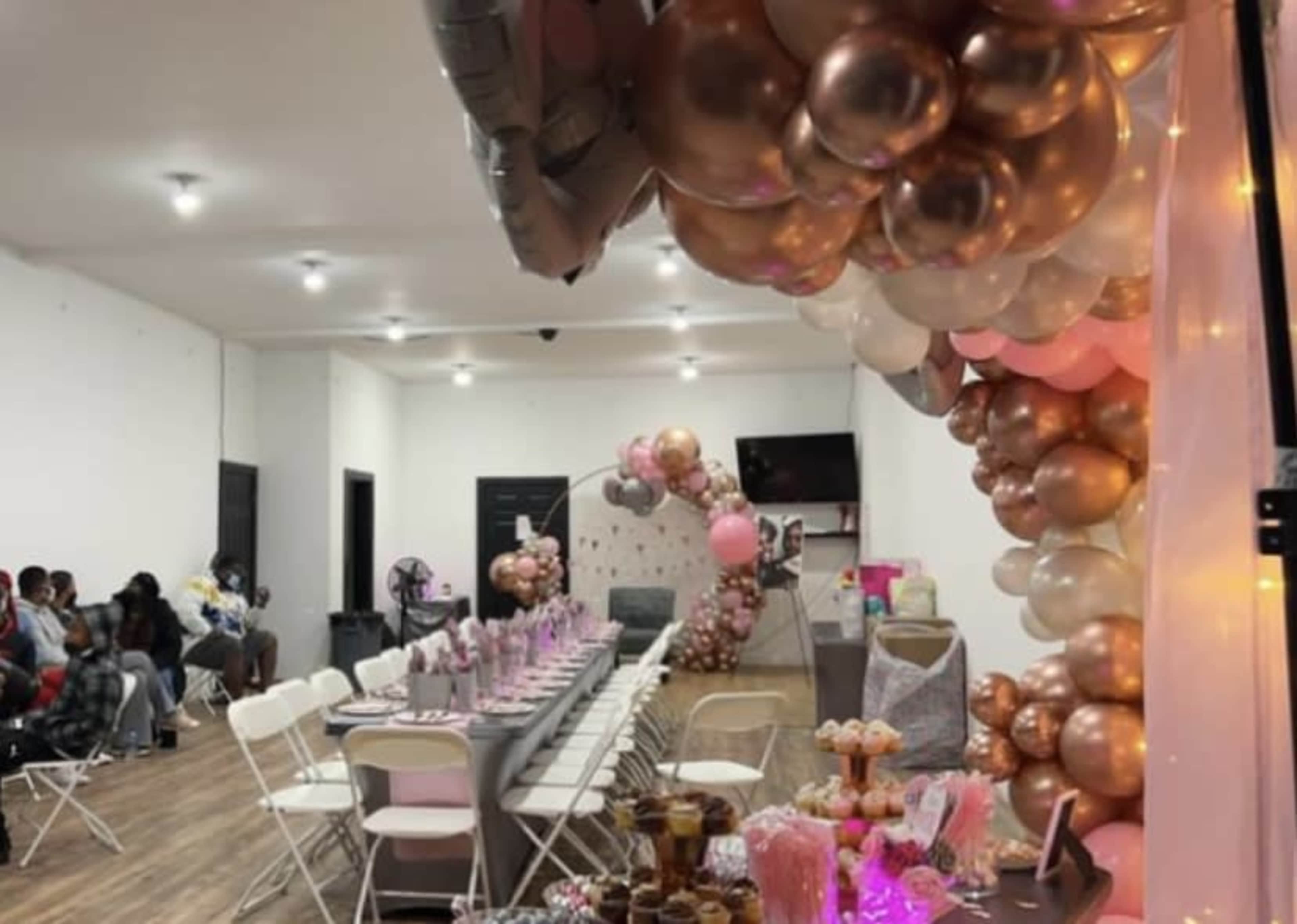 A decorated indoor event space with a long table set for guests and an array of colorful balloons arching over the setting.