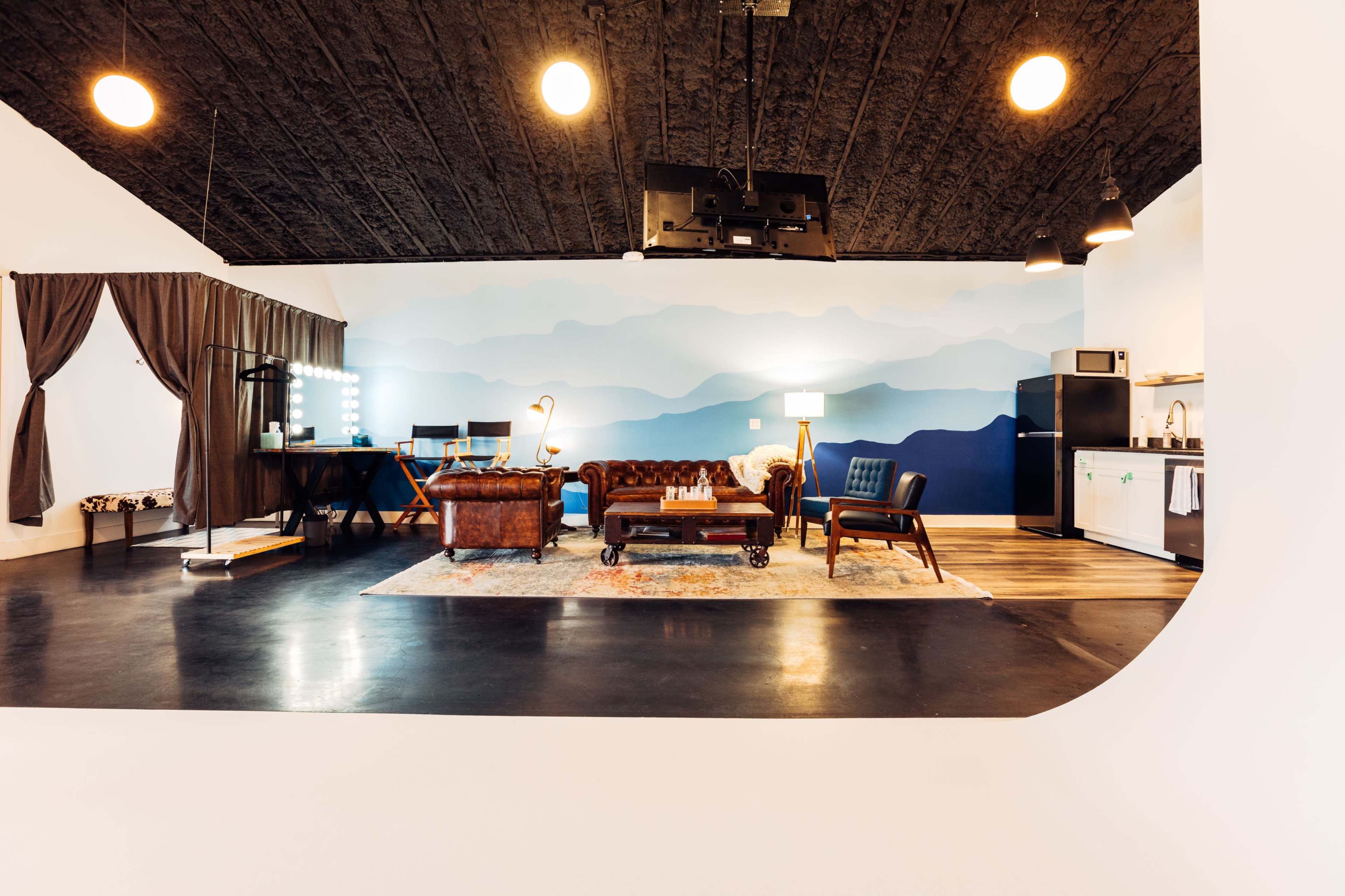 The image depicts a modern interior space featuring a lounge area with a leather couch, a blue accent wall, and various furnishings including a table and lighting fixtures.