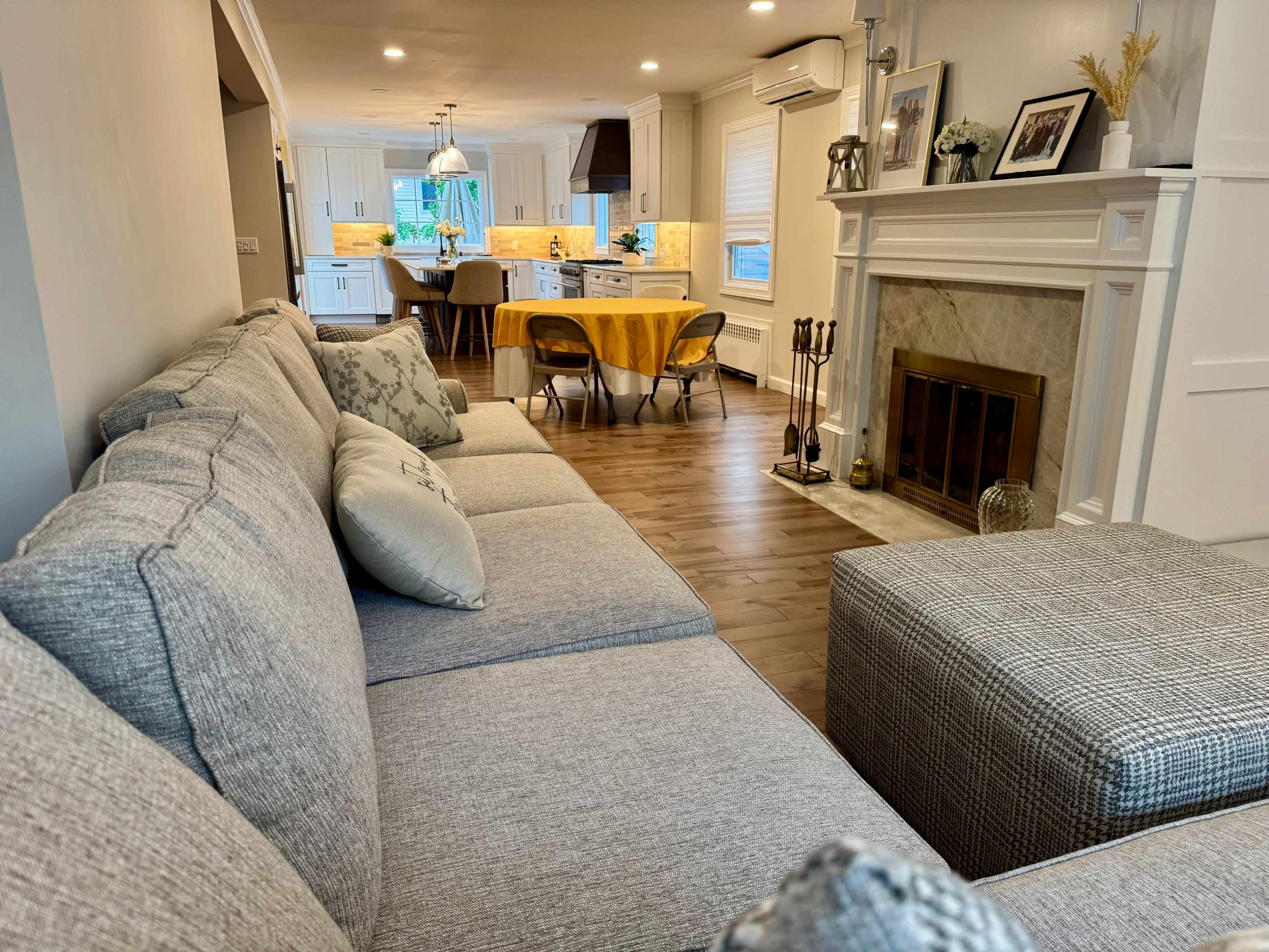A spacious living room features a sectional sofa, a fireplace, and a view of a kitchen with a dining area.