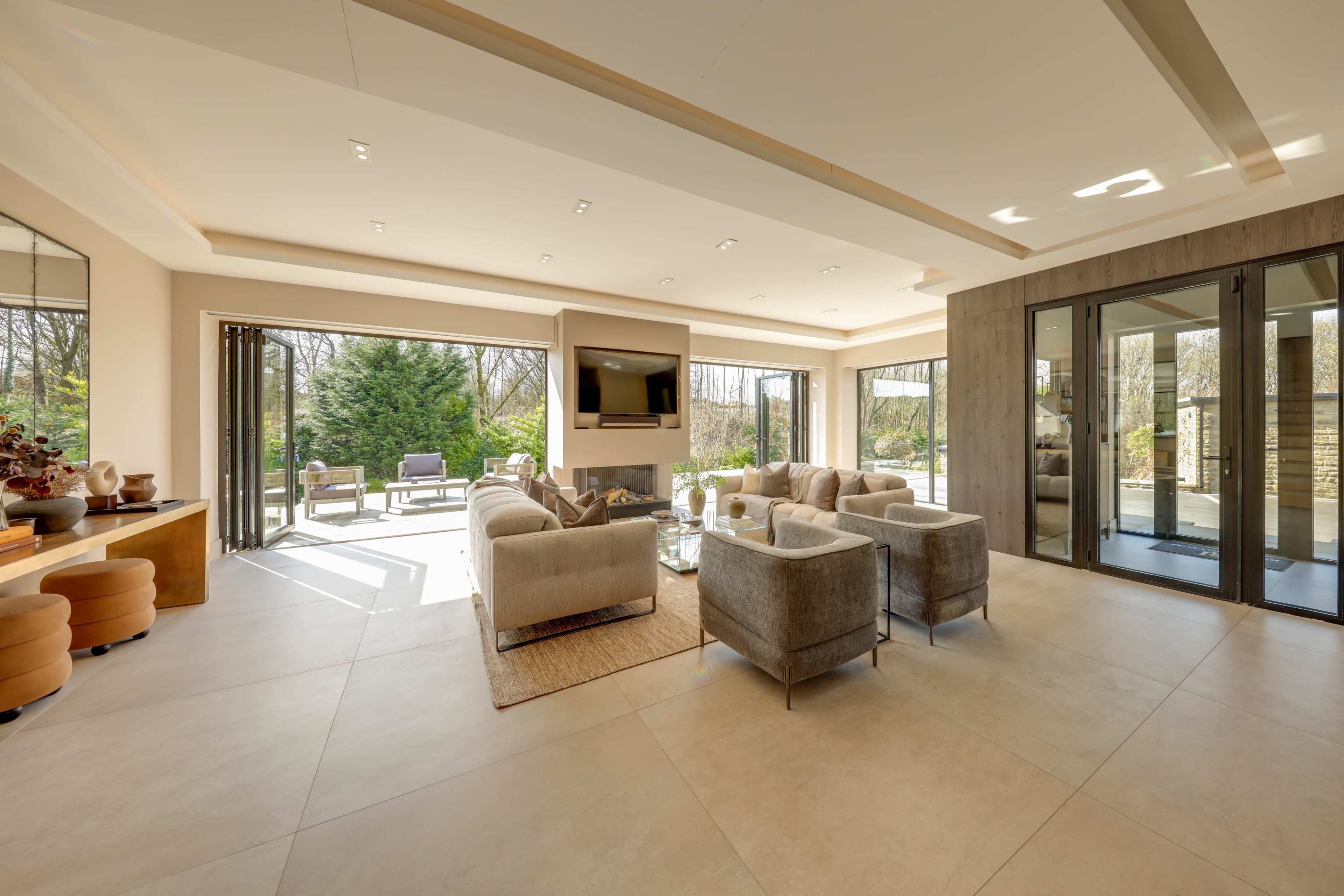 A spacious living area features modern furniture, large windows, and access to an outdoor patio surrounded by greenery.
