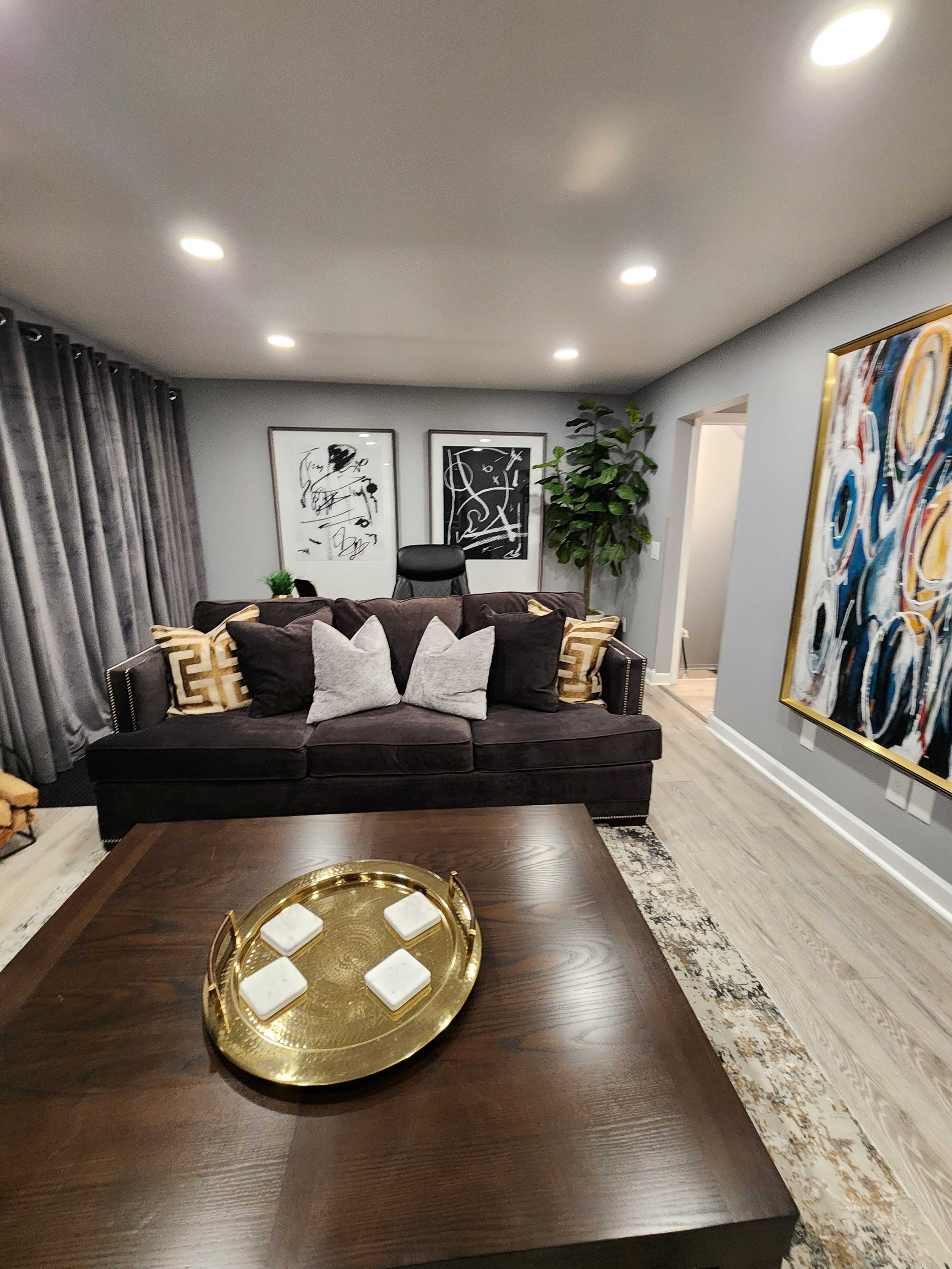 A modern living room featuring a dark sofa with decorative pillows, a wooden coffee table with a tray, and abstract wall art.