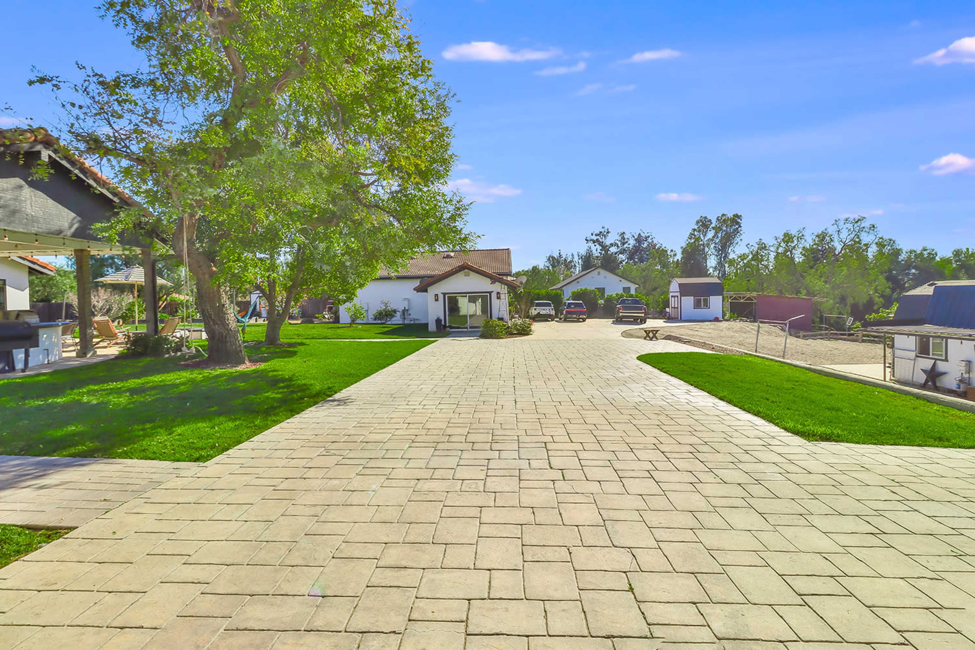 A paved driveway leading to several buildings and parked vehicles in a landscaped area with trees and grass.