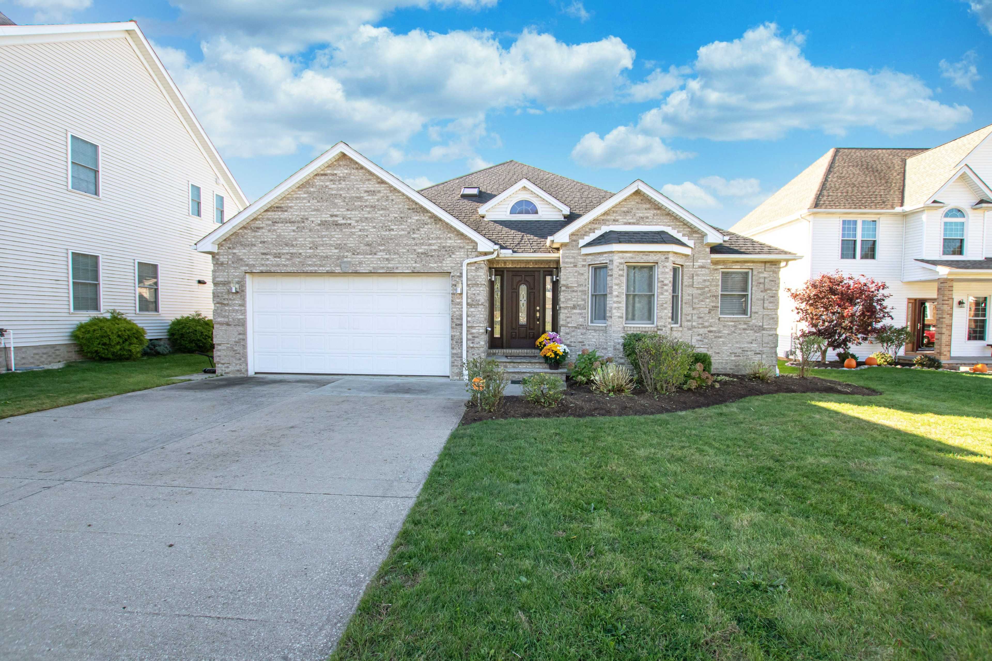 A single-story house with a stone facade and a double garage, surrounded by a well-maintained lawn and garden.