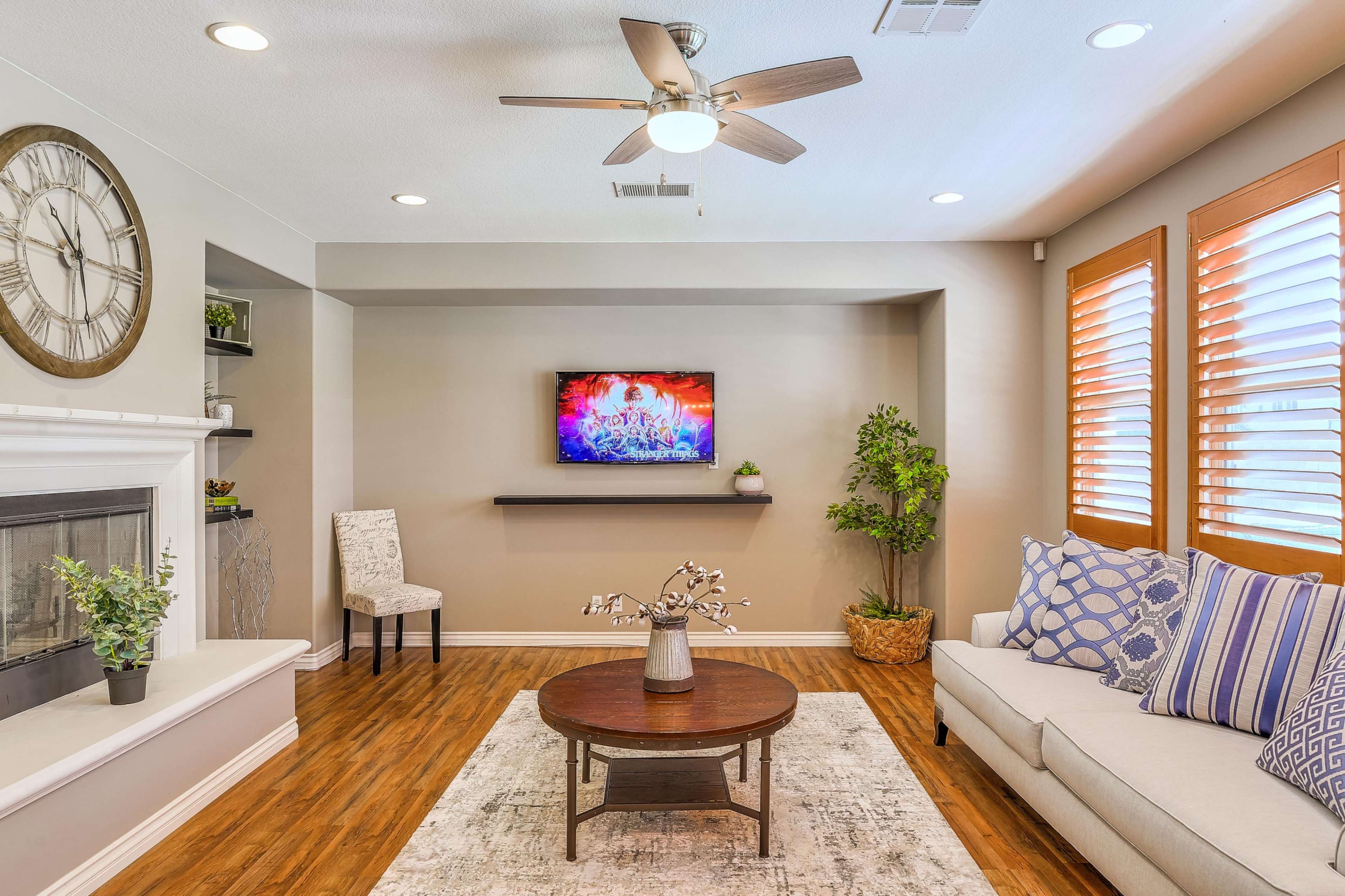 A modern living room with a ceiling fan, a wall-mounted TV, a round coffee table, and a sectional sofa placed on a rug.