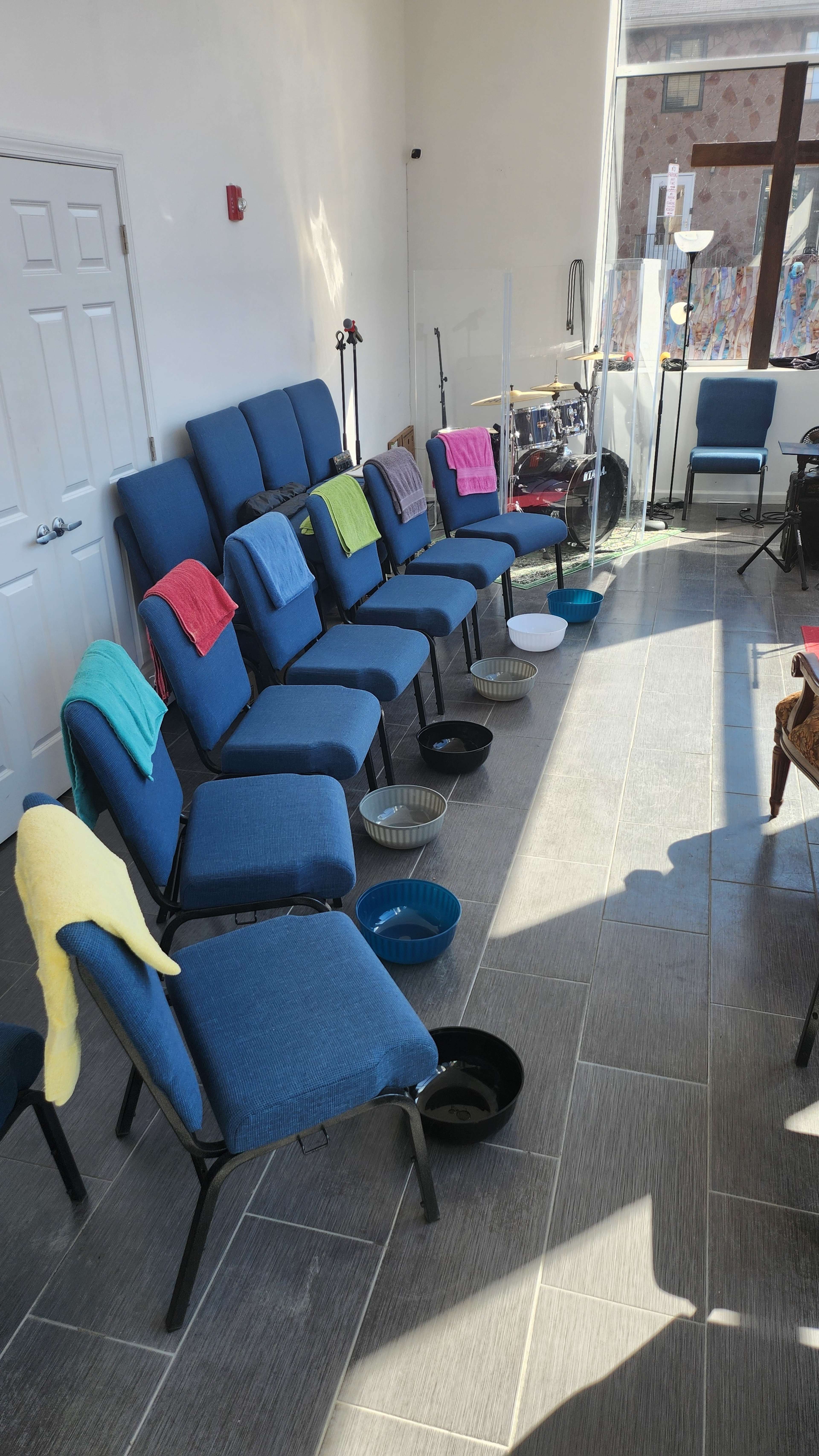 The image shows a row of blue chairs with colorful towels draped over the backs, positioned near several bowls on the floor in a brightly lit room.