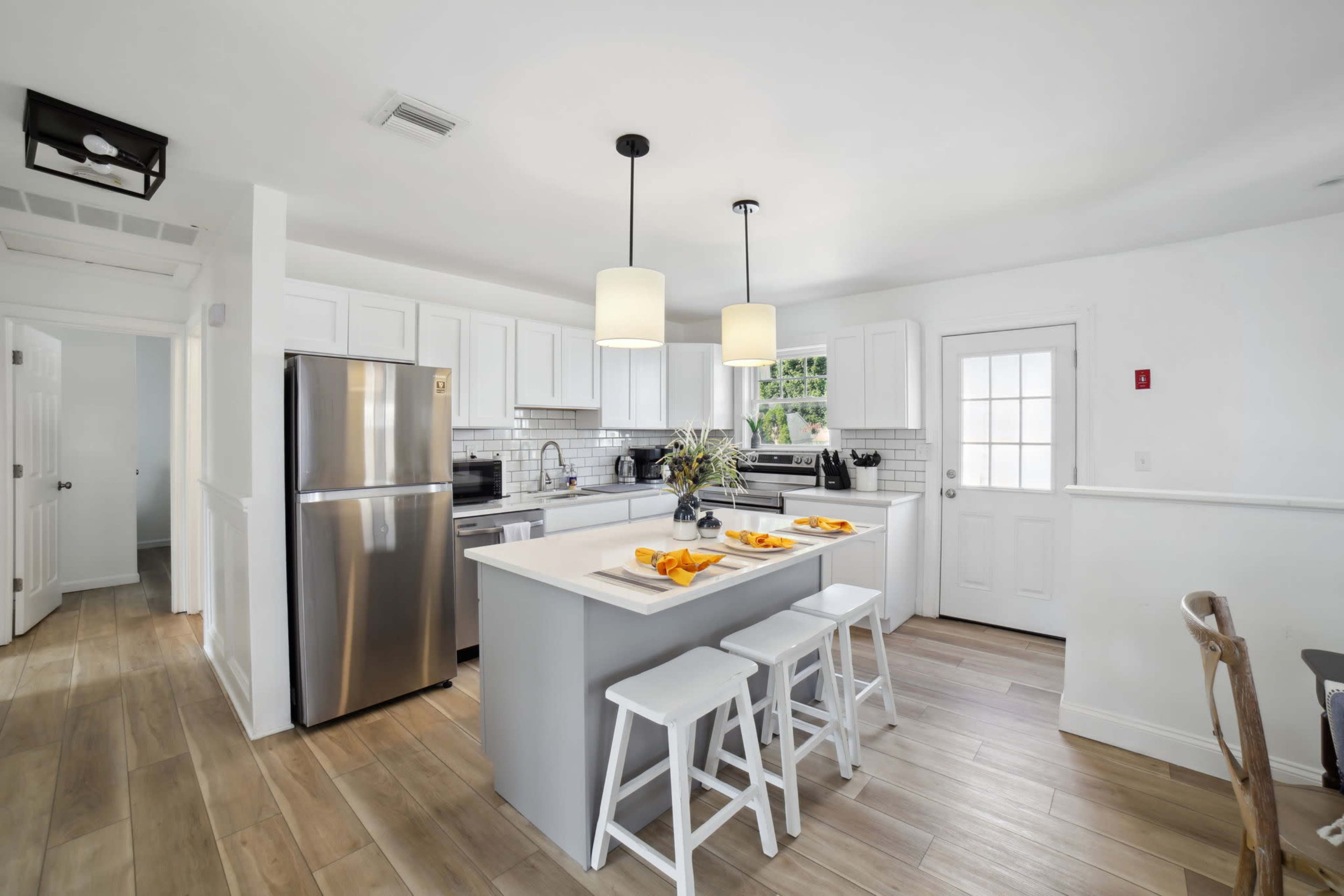 A modern kitchen features white cabinetry, stainless steel appliances, and a centered island with seating for three.