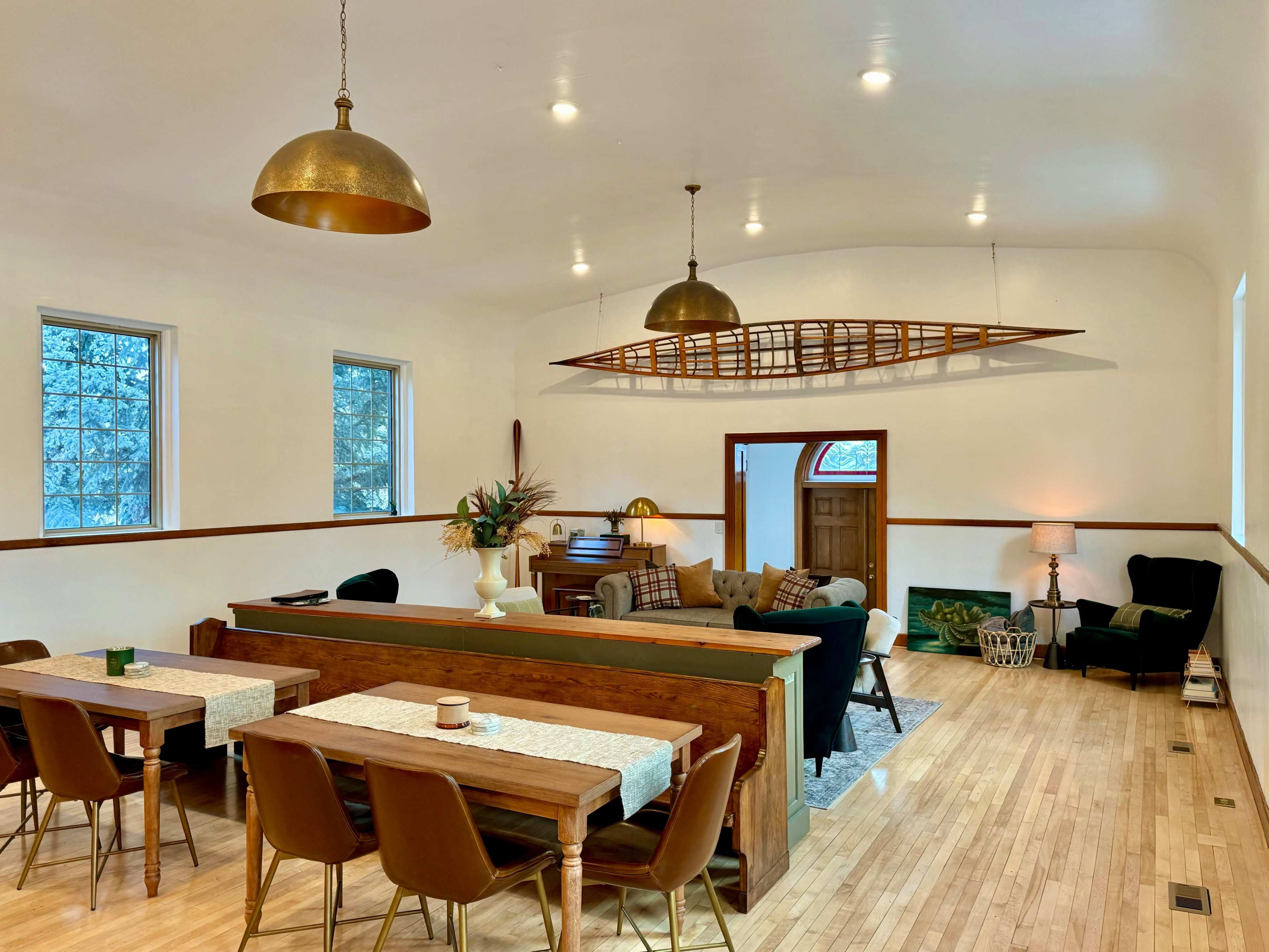 A spacious interior with a dining area featuring wooden tables and chairs, and a cozy living area with a black sofa and a decorative canoe mounted on the wall.