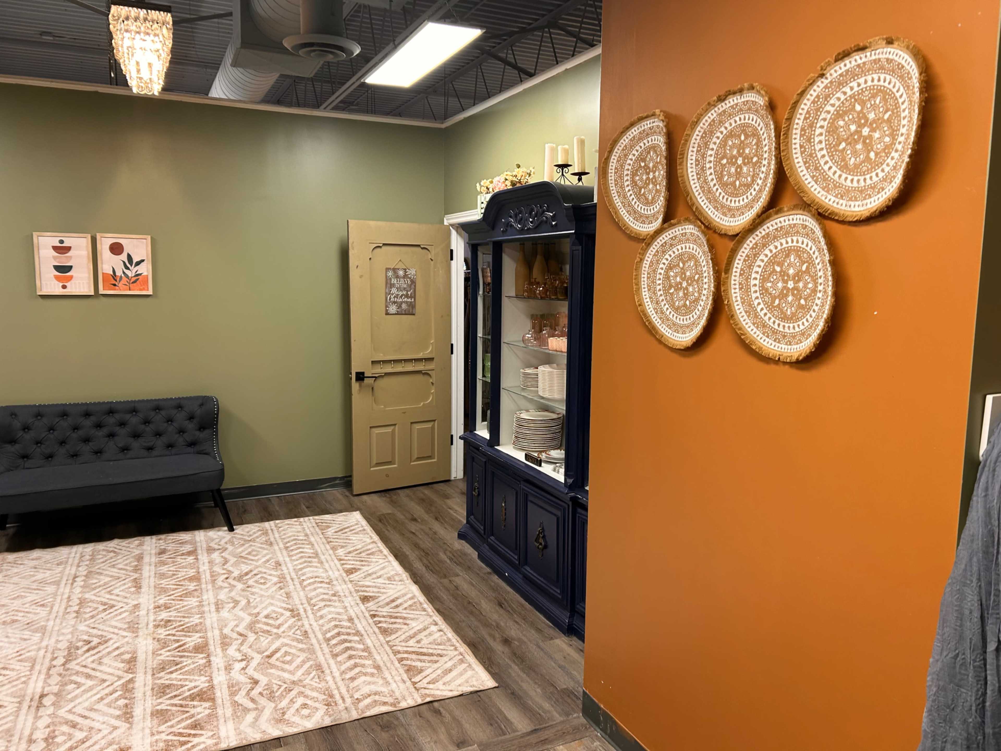 The image shows a cozy room with a dark blue cabinet and decorative wall hangings, featuring a tufted sofa, a patterned rug, and a partially open door.