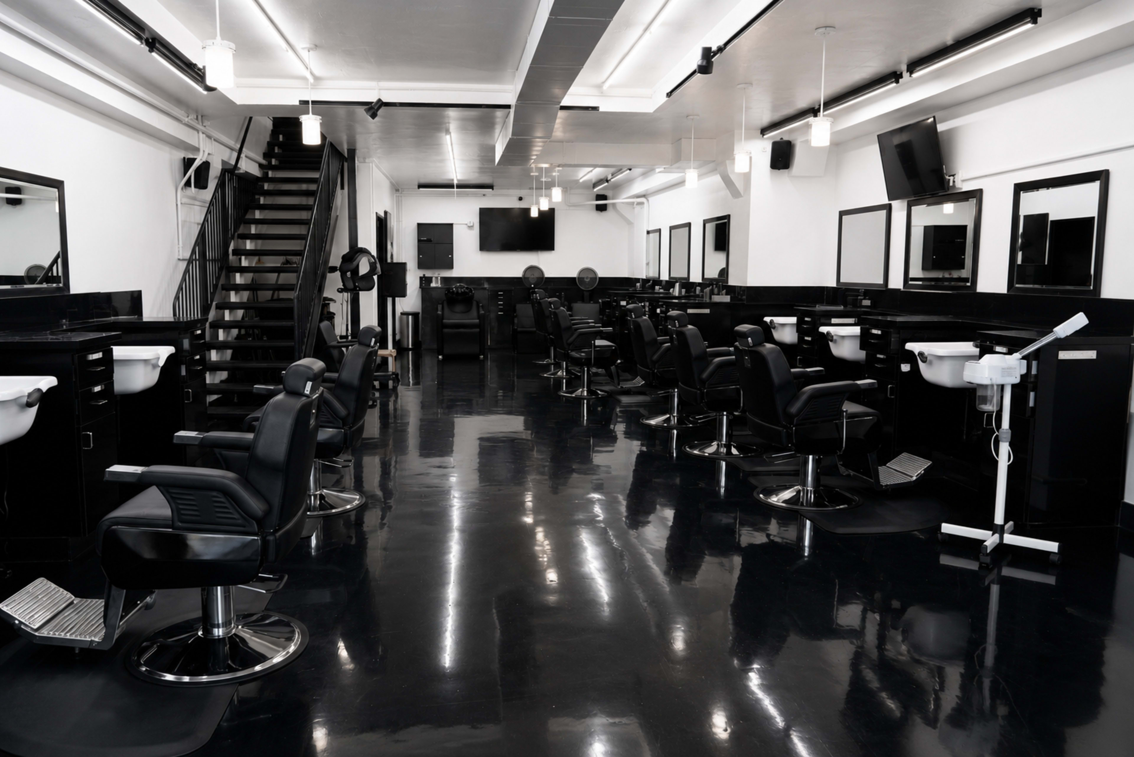 The image shows a modern, spacious hair salon with black styling chairs, mirrors, and sinks arranged neatly along the walls and rows of lights above.
