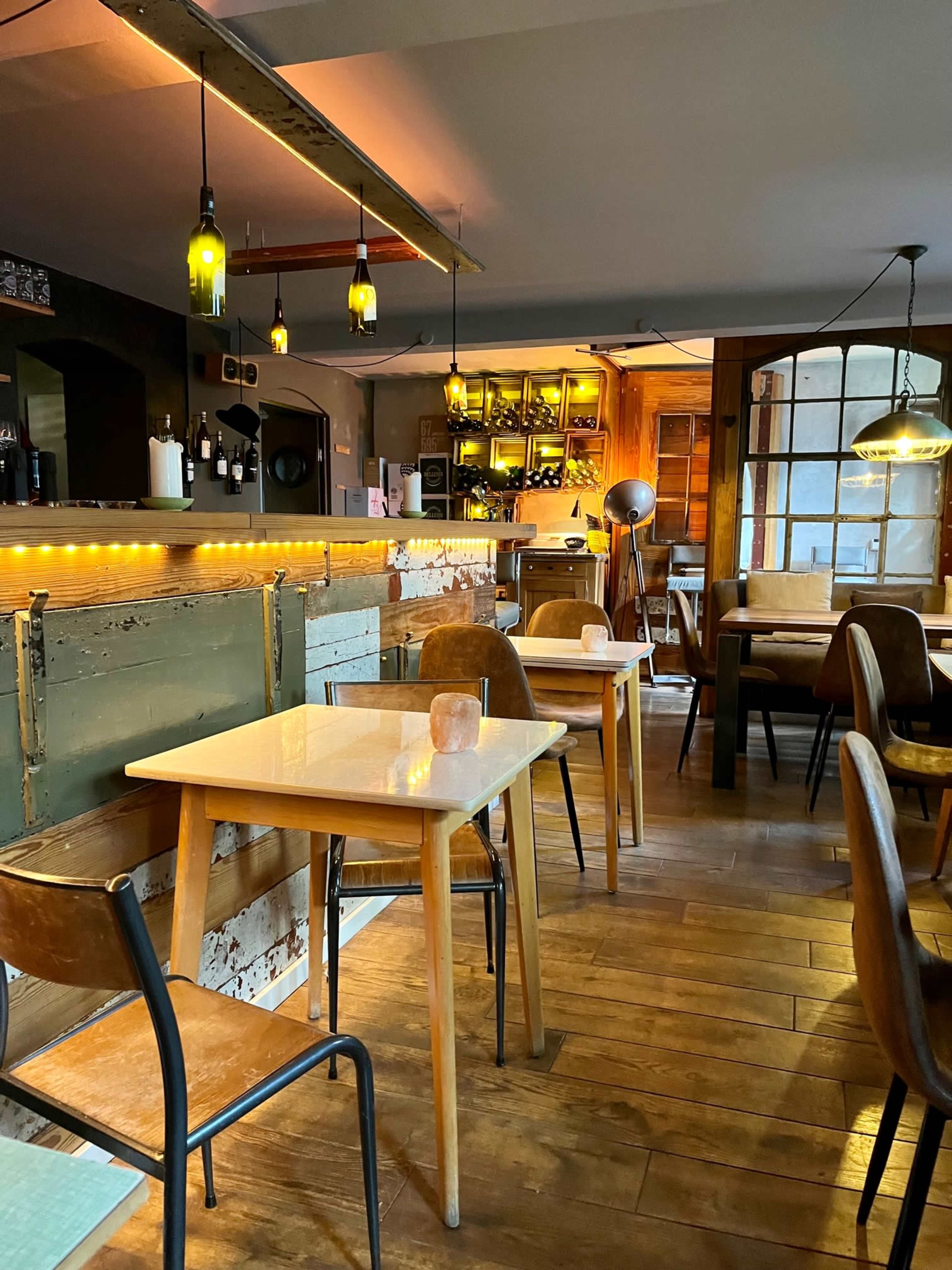 A cozy restaurant interior with wooden floors, simple tables, and warm lighting fixtures.