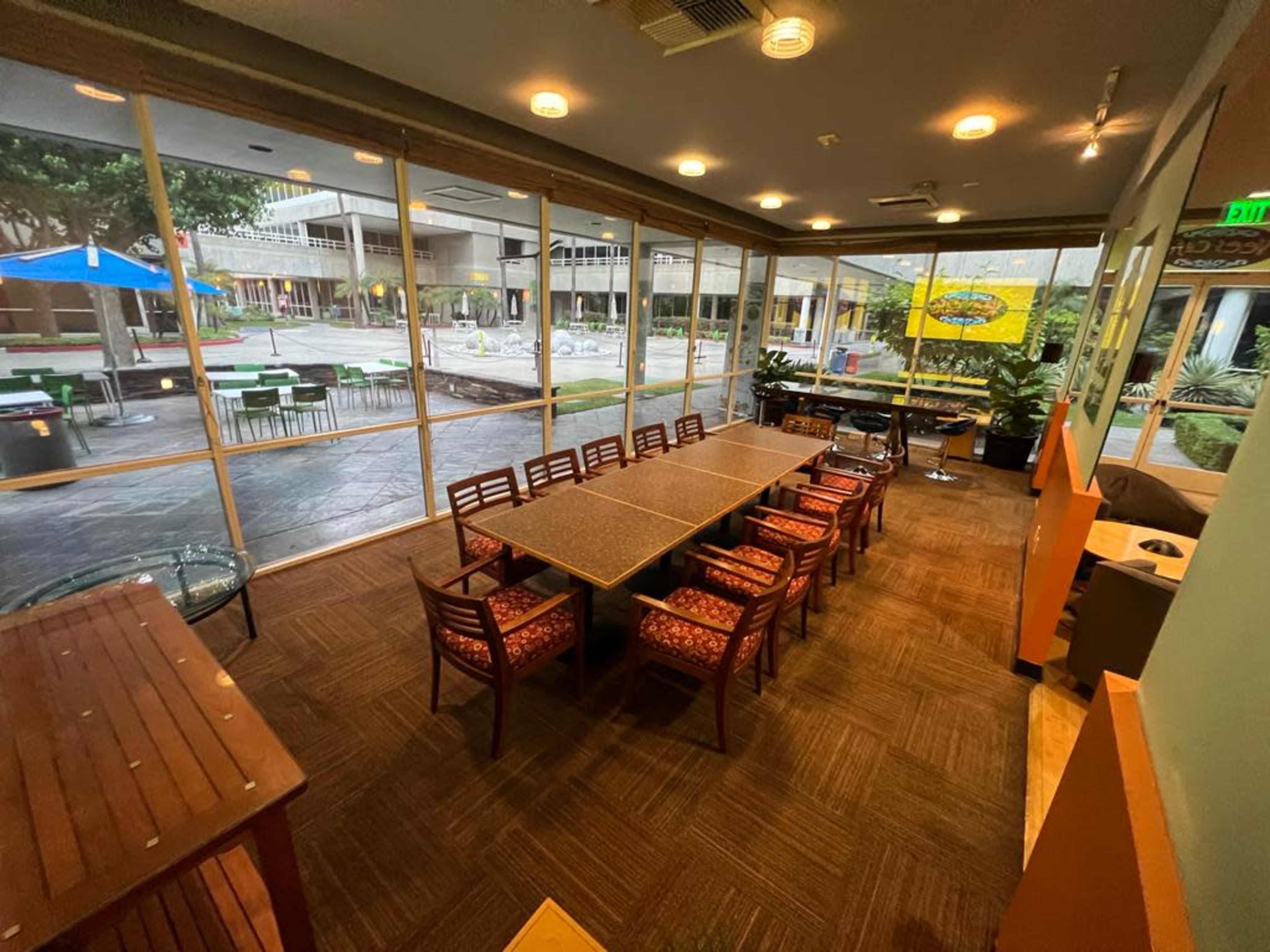 A spacious indoor meeting area with a long table and chairs, overlooking an outdoor courtyard through large glass windows.