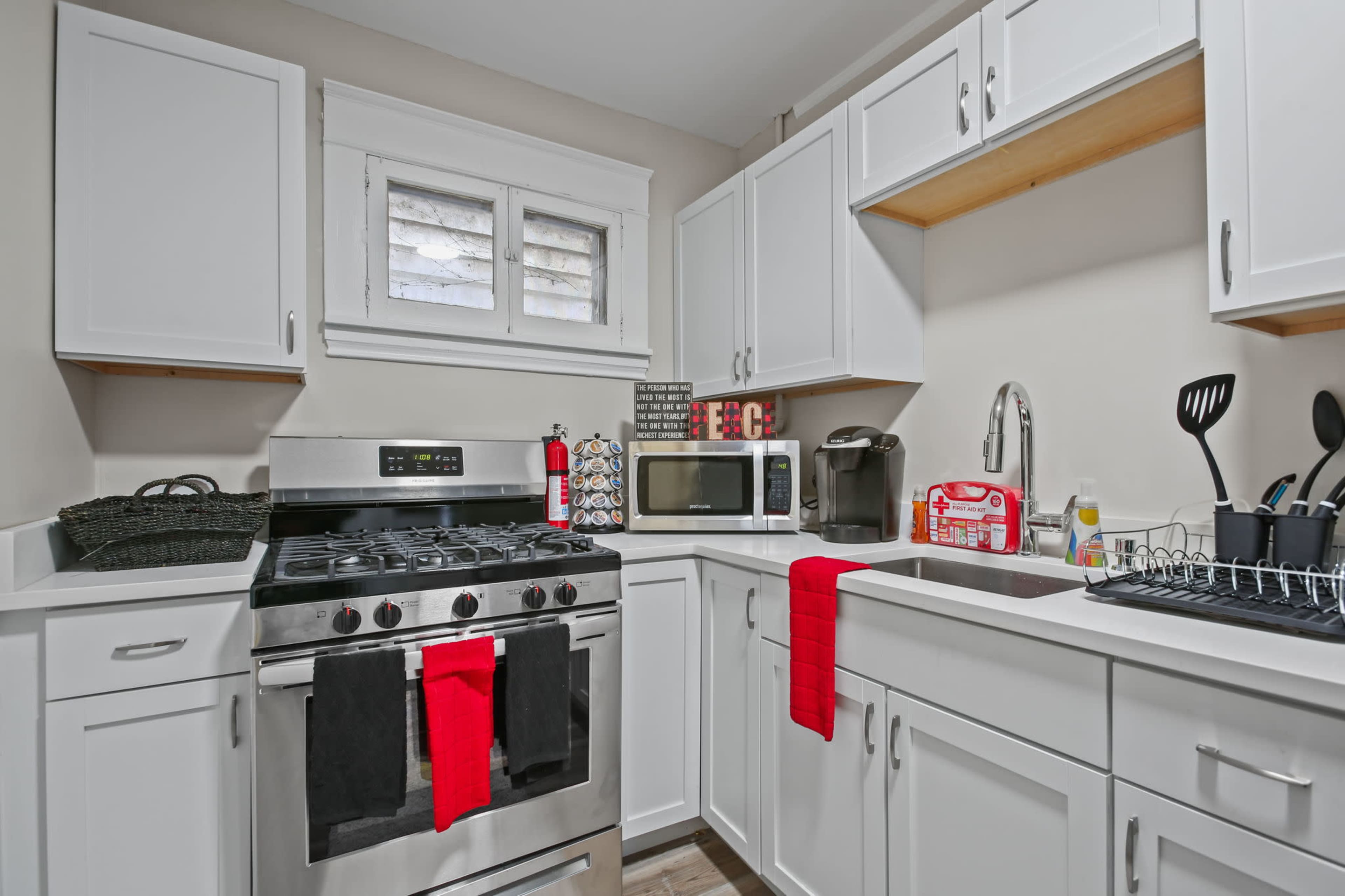 A compact kitchen with white cabinetry, a stainless steel stove, a microwave, and a sink with kitchen utensils on the counter.